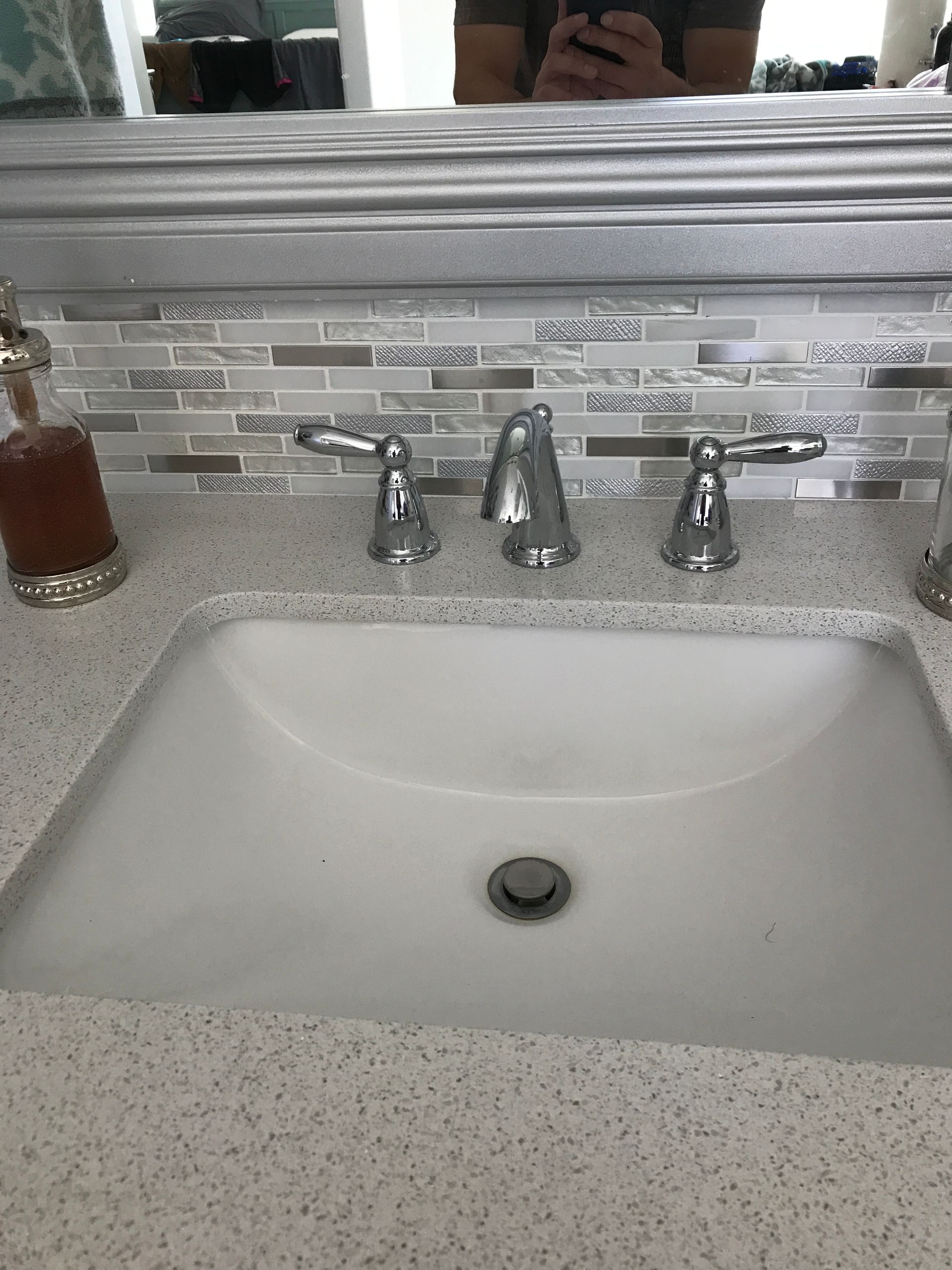 Bathroom sink with chrome faucet and speckled countertop beneath a mosaic tile backsplash and mirror