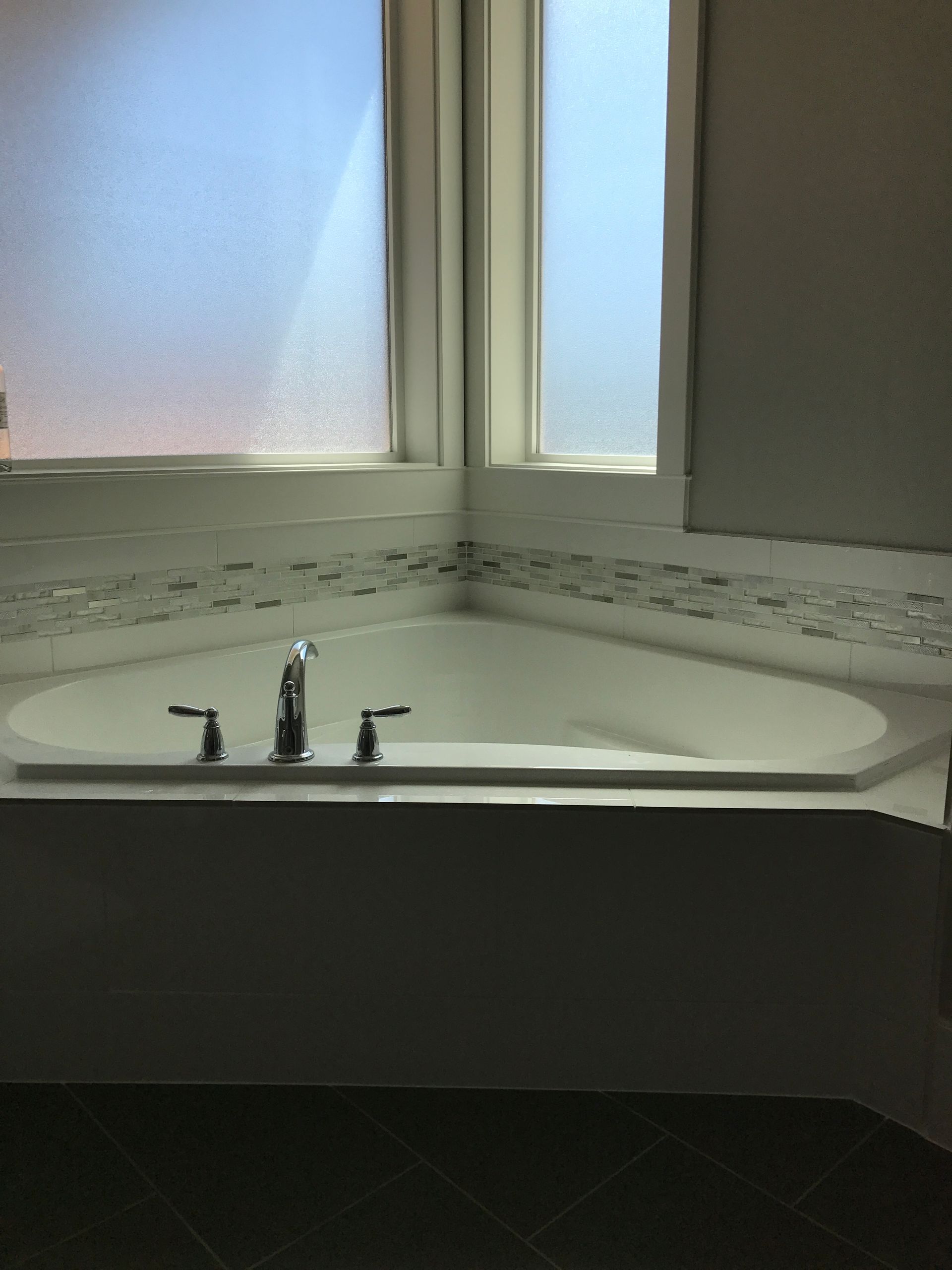 Bathroom sink and mirror beneath frosted windows, with a dark countertop and chrome faucet.