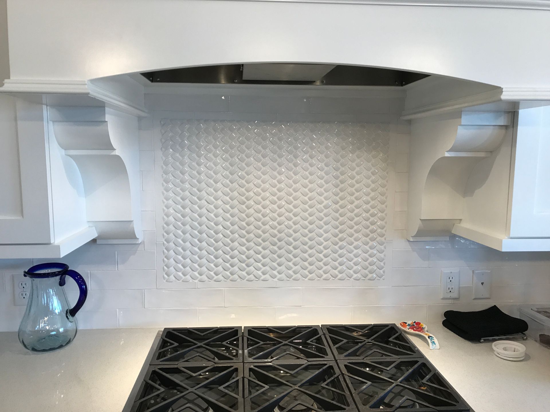 Kitchen stove with white tile backsplash, stainless hood, and a blue glass bottle on the left.
