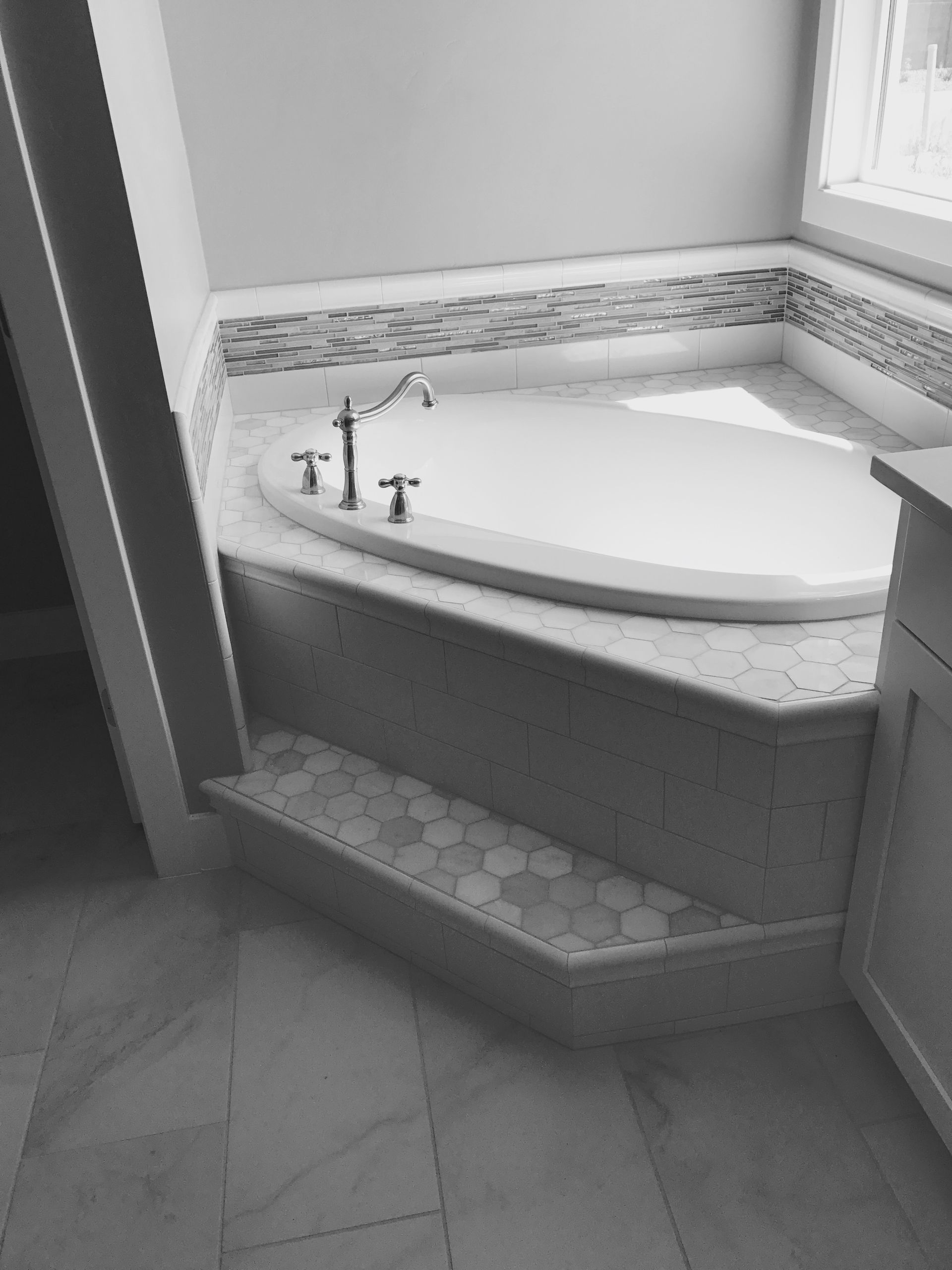 Bathroom corner with a white bathtub, built-in ledge, and tiled floor by a window.