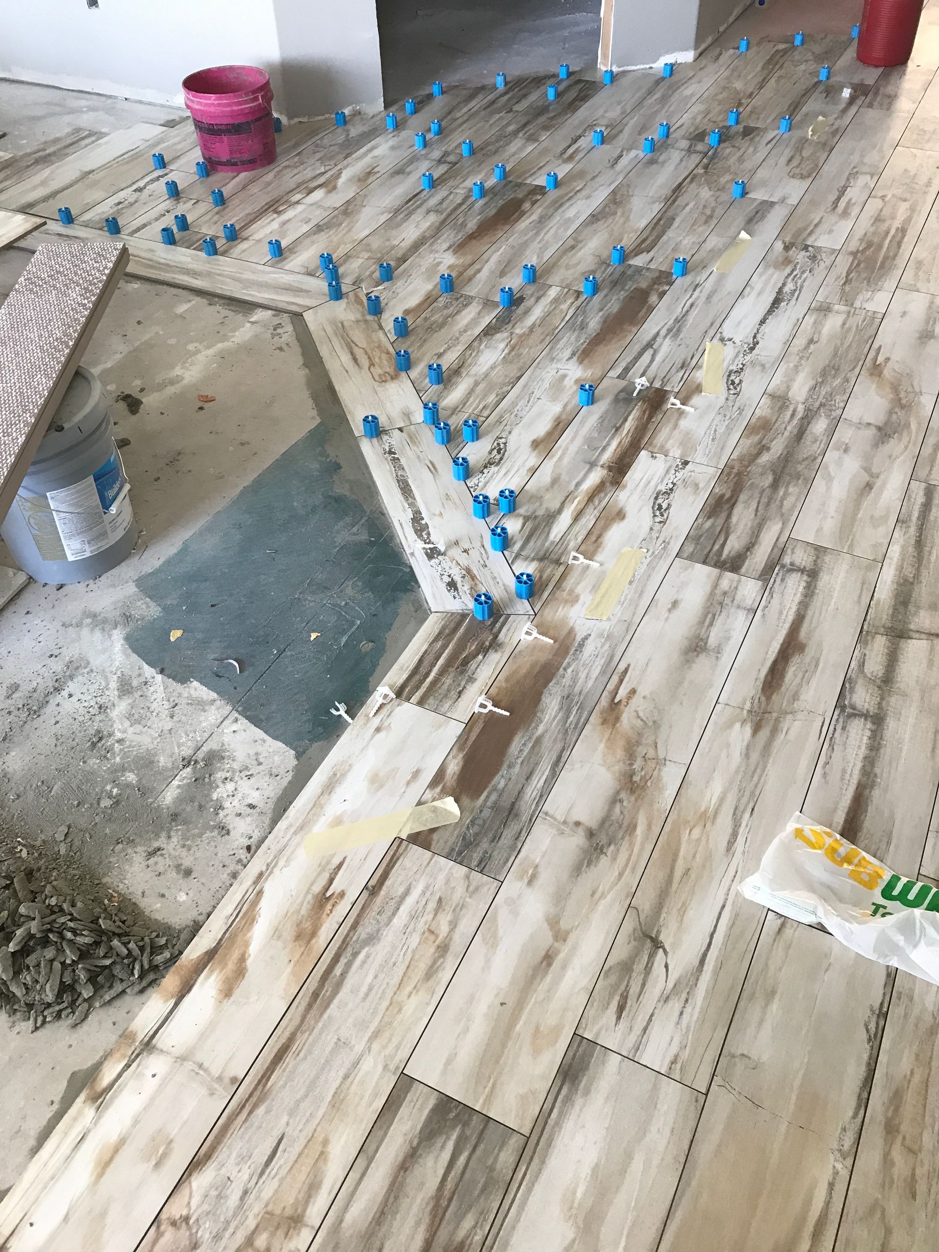 Partially tiled floor under renovation with blue spacers and a bucket on the left