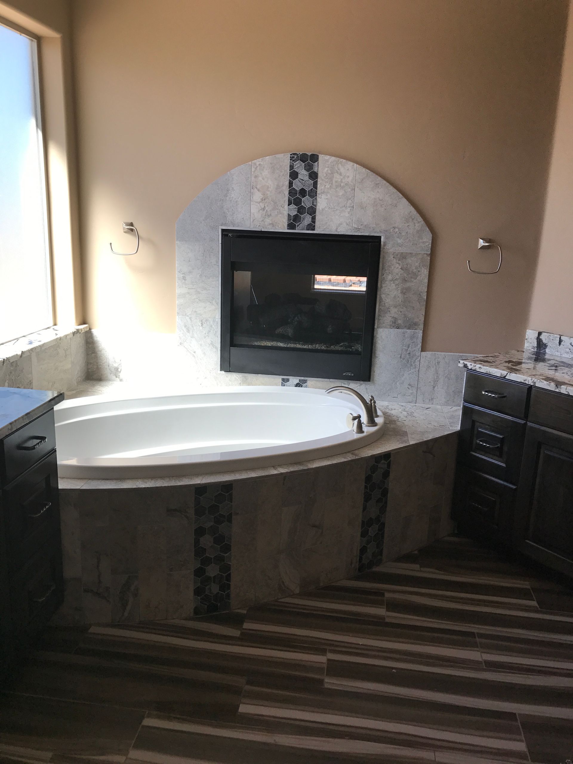 Bathroom with corner soaking tub, tiled fireplace, and dark vanity cabinets.
