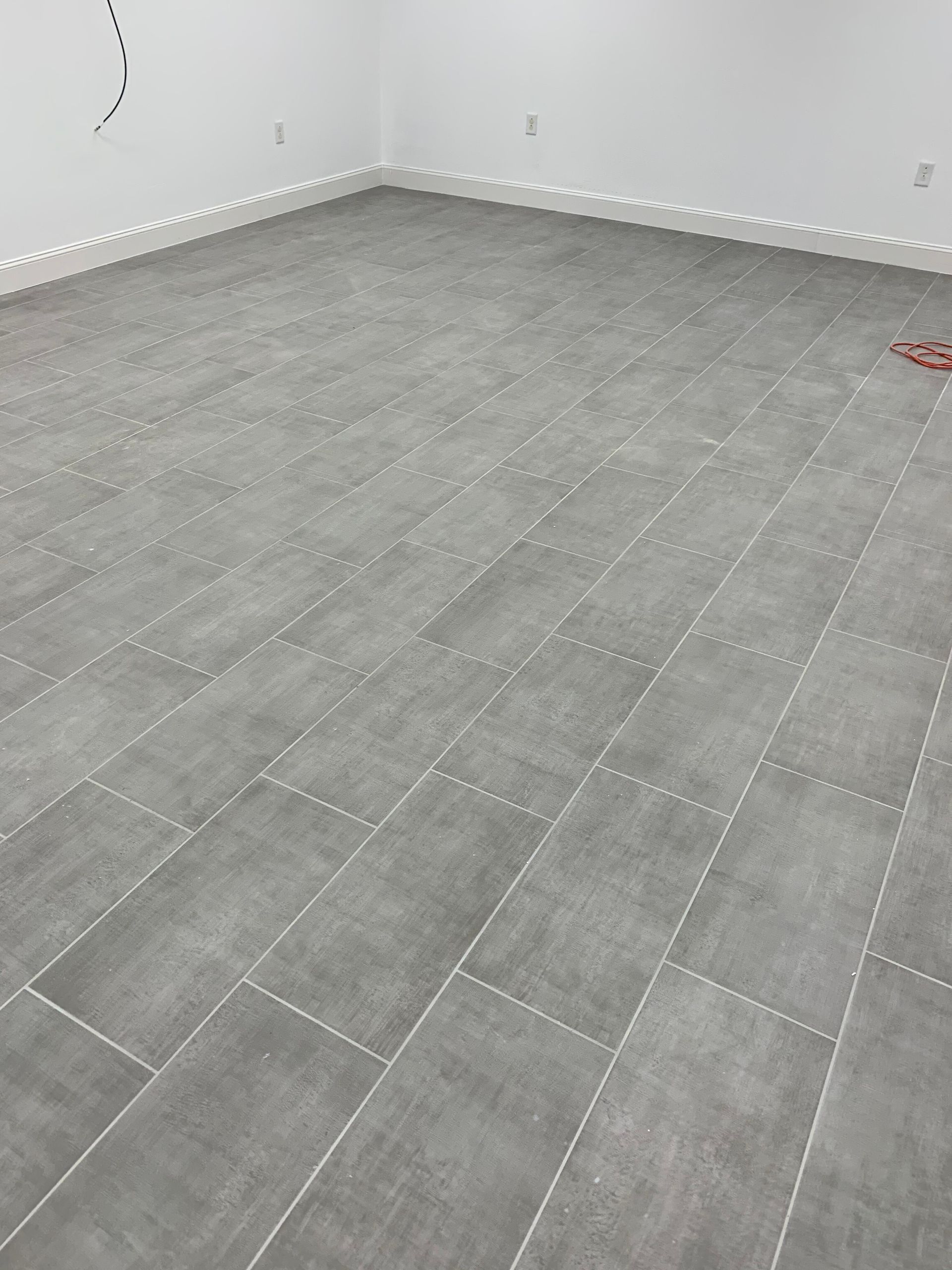 Empty gray-tiled room with white walls and baseboards, seen from a corner view