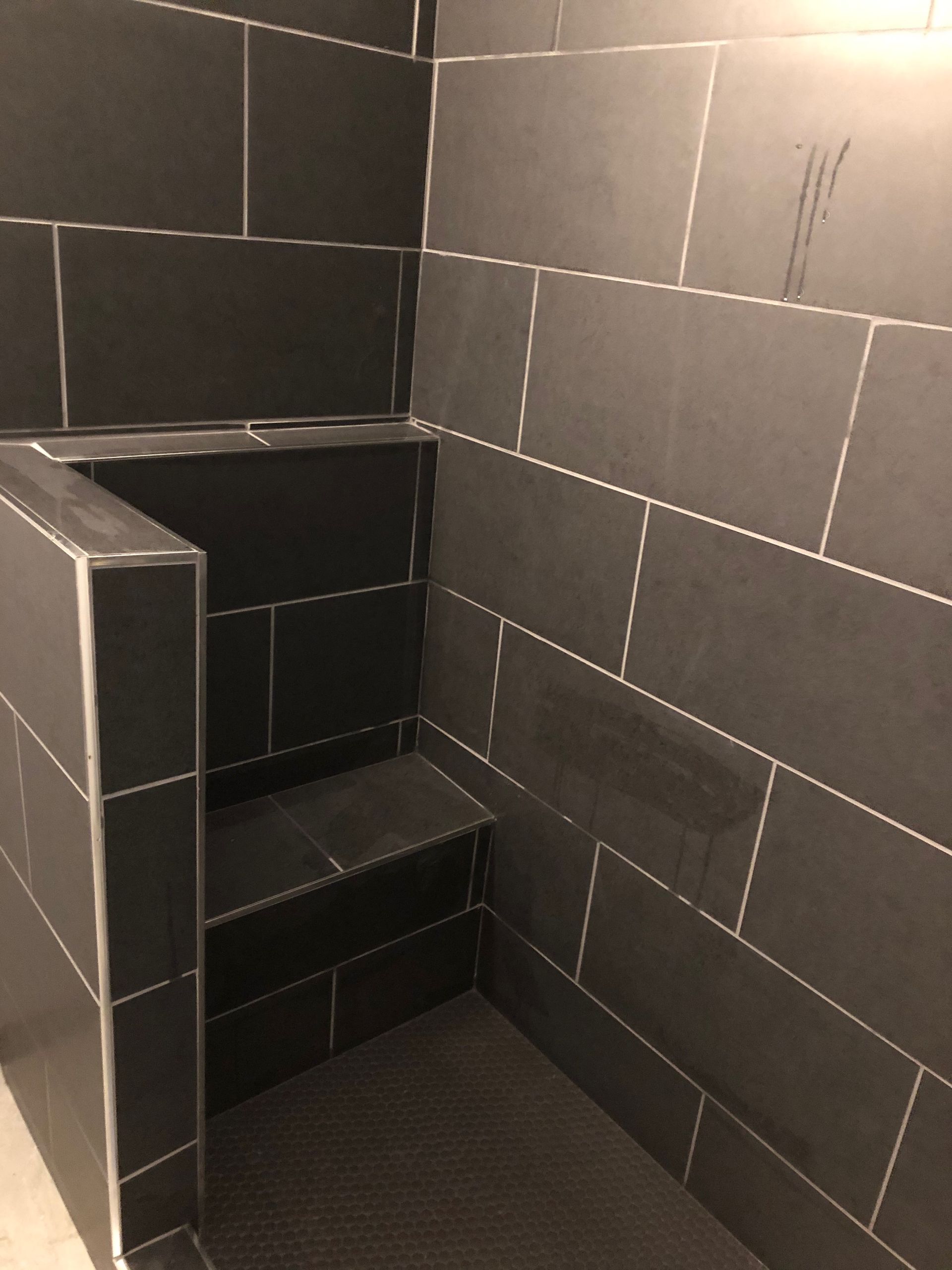 Small tiled shower stall with built-in seat and dark gray walls.