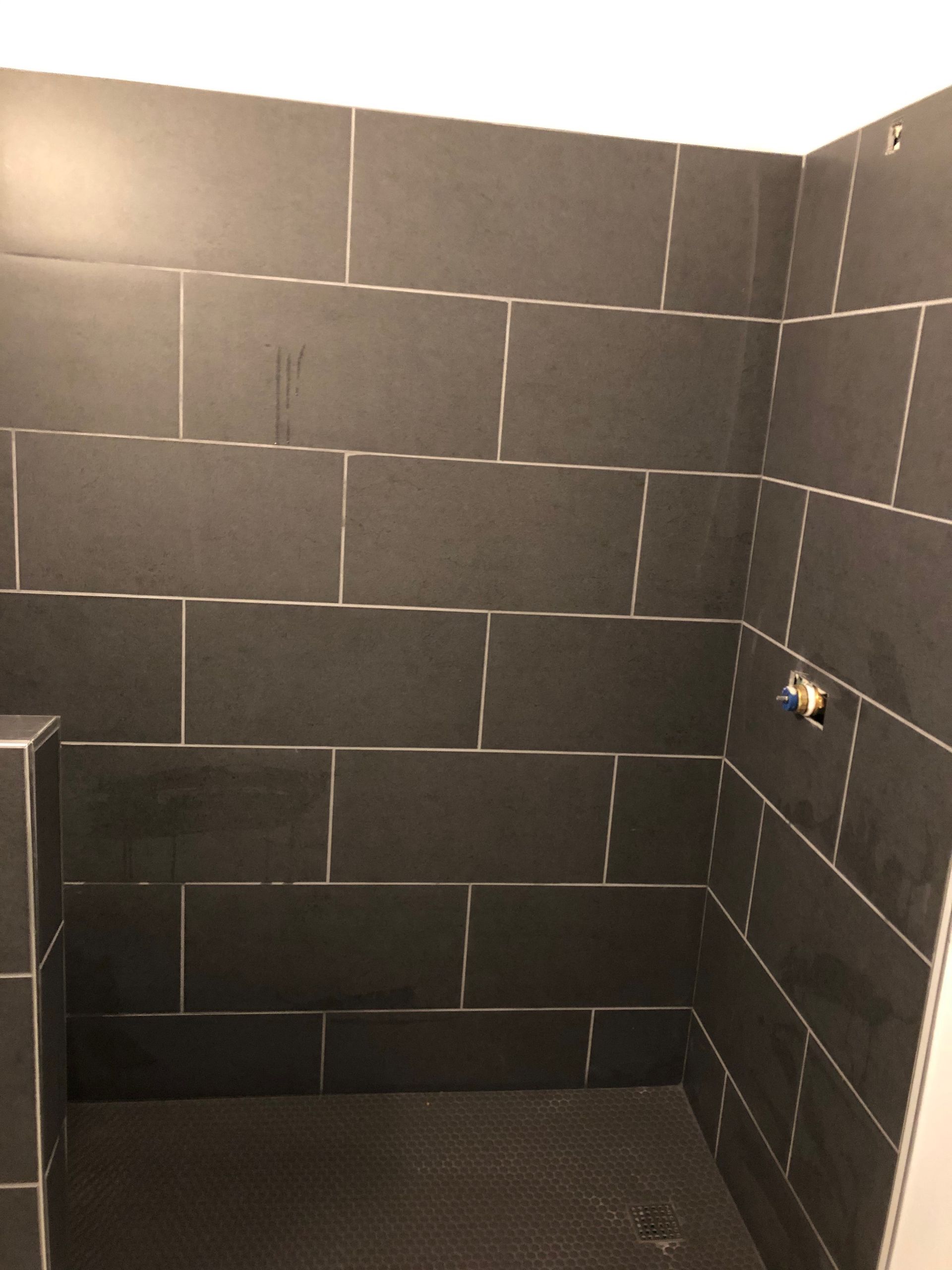 Empty tiled shower stall with dark gray walls and floor, and a chrome shower fixture on the right.