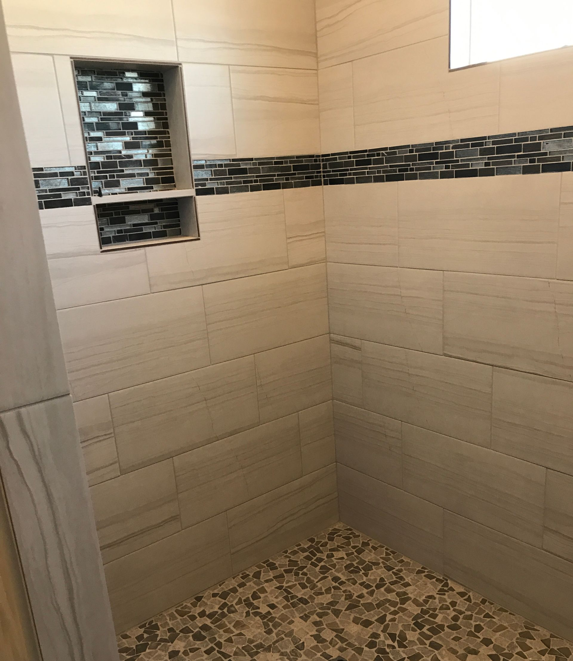 Tiled shower stall with beige walls, dark decorative border, and pebble-pattern floor.