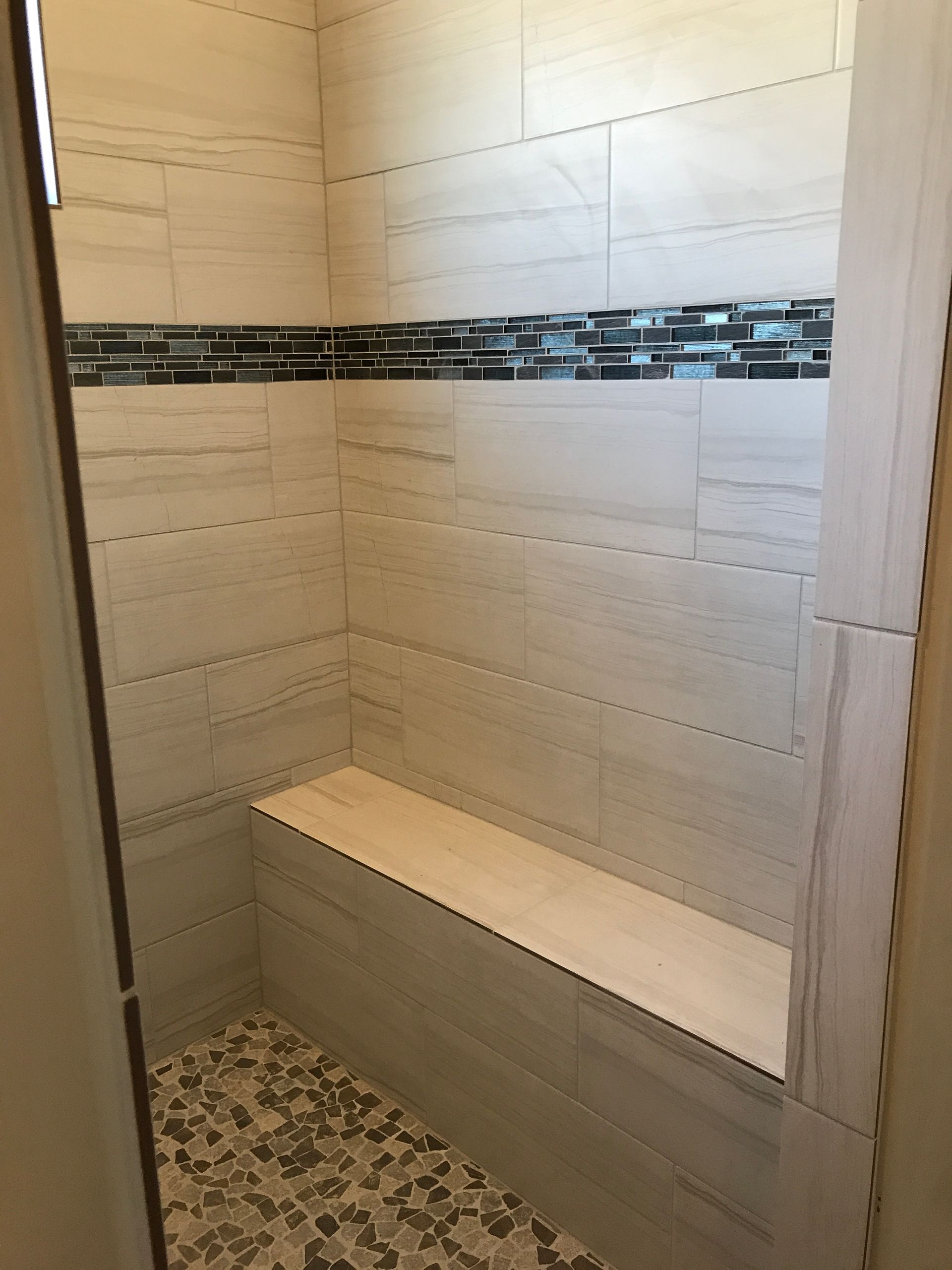 Small tiled shower nook with a built-in bench and decorative mosaic accent strip.