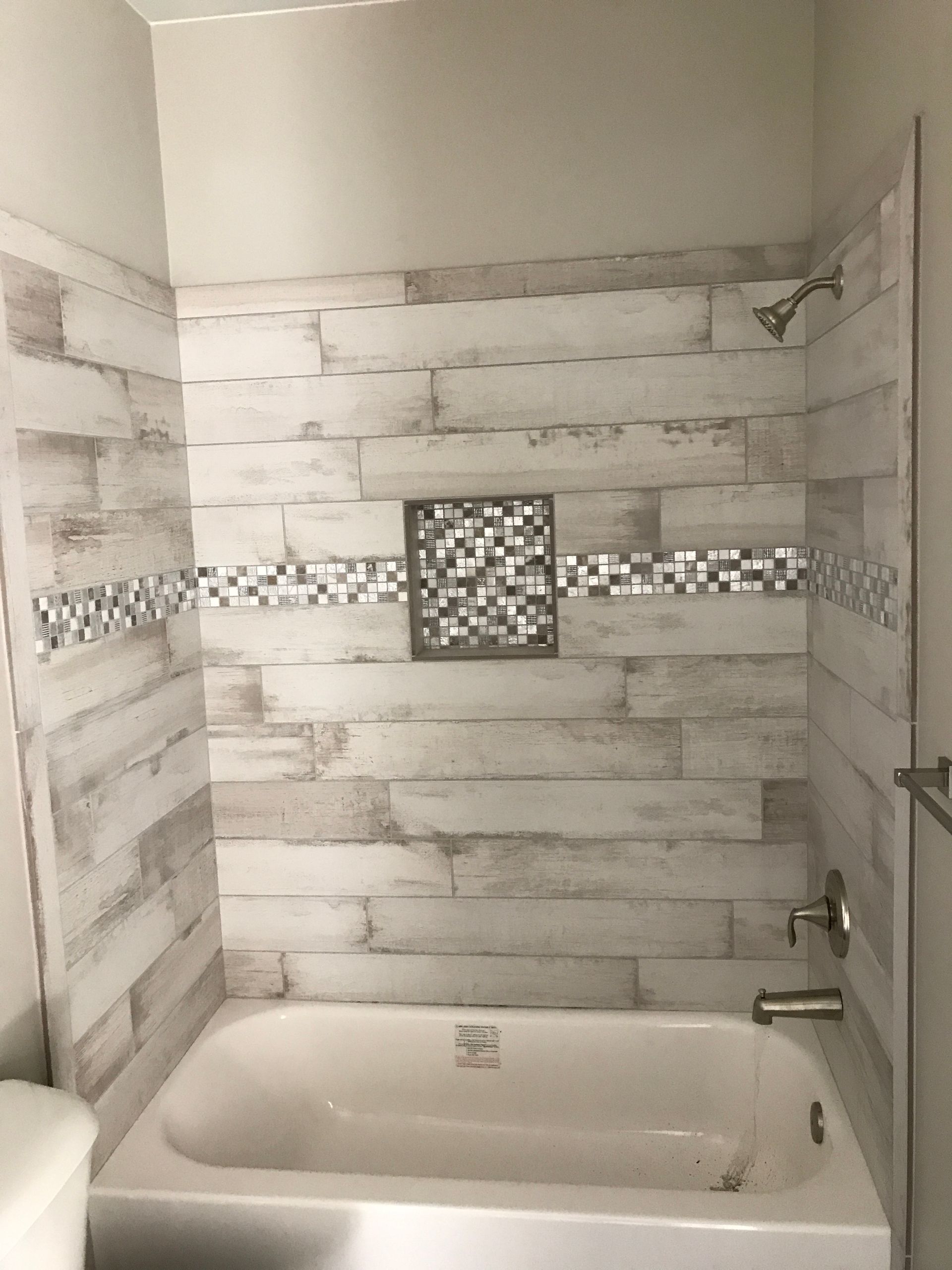 Small tiled bathroom with a white tub, decorative wall tile band, and a built-in niche above the tub.