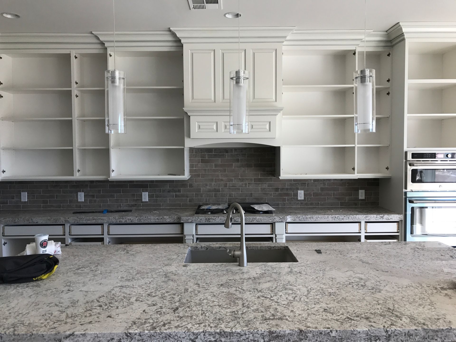 Modern kitchen with white cabinets, dark backsplash, granite island, and built-in ovens