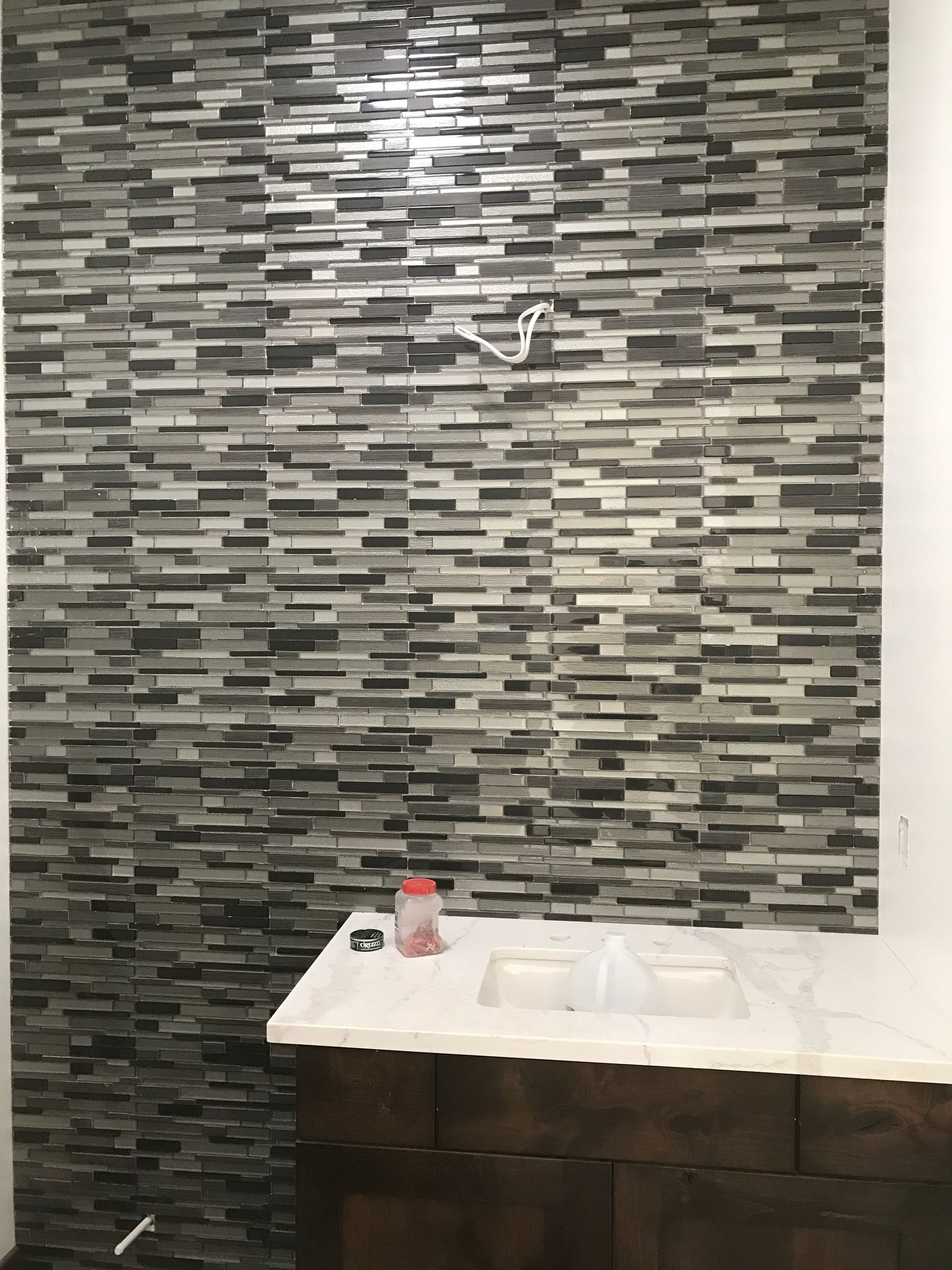 Bathroom vanity with white sink, dark wood cabinet, and gray mosaic tile wall