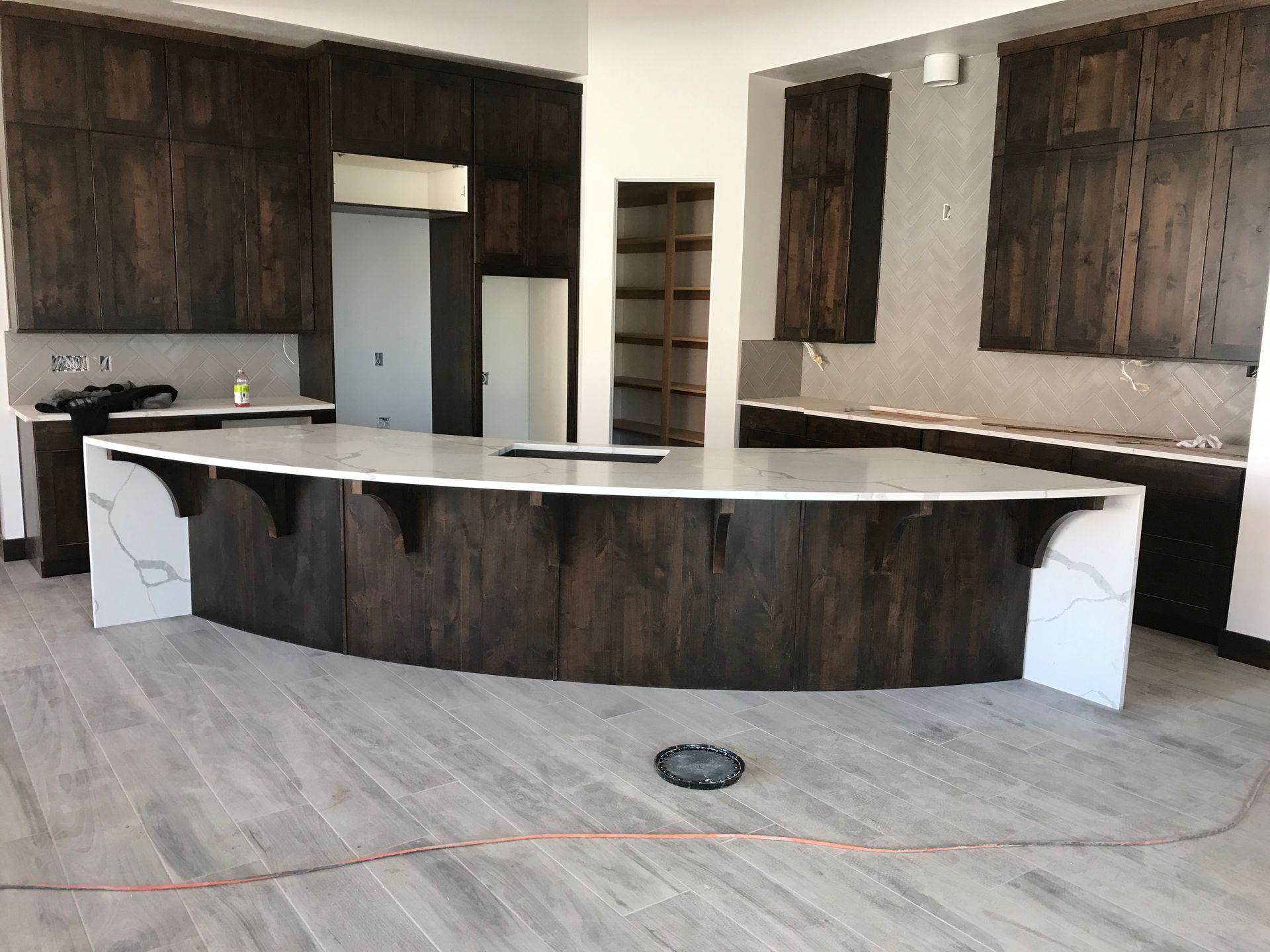 Empty kitchen with dark wood cabinets, white countertops, and a large curved island under construction