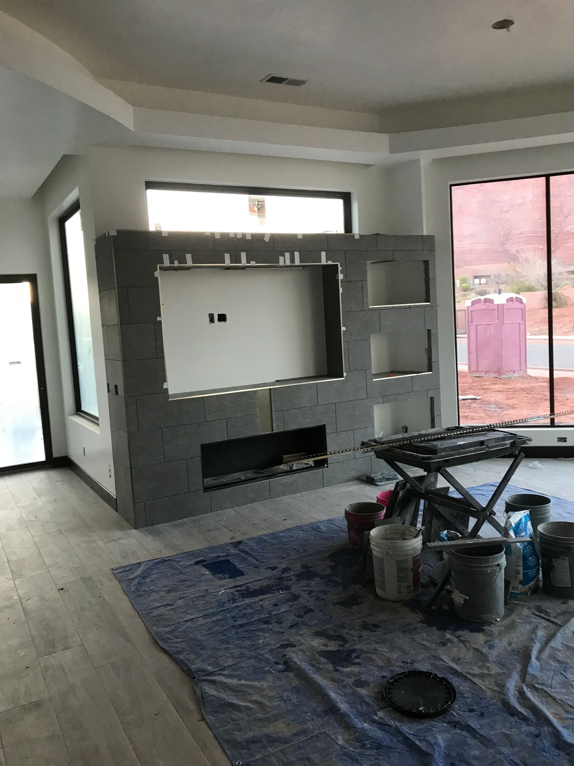 Partially renovated living room with a gray brick fireplace, rug, and construction tools on the floor