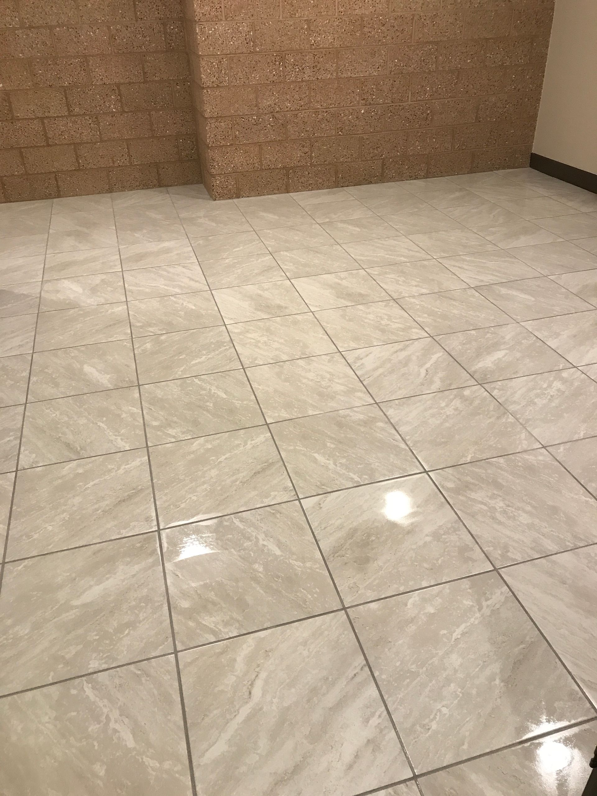 Empty tiled floor with beige walls and bright reflections from overhead lights.