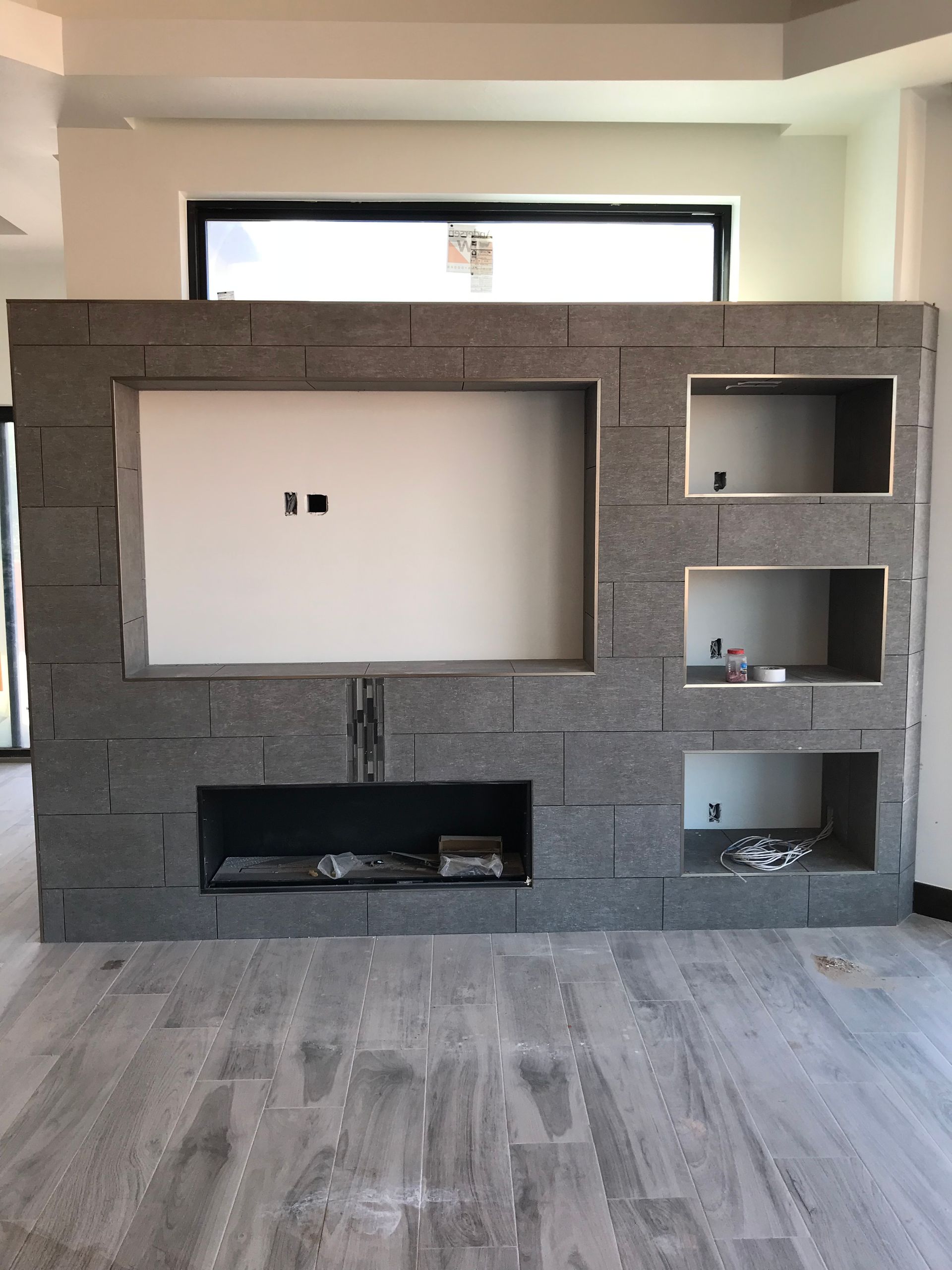 Unfinished gray concrete fireplace wall with built-in niches in a modern room, wood-look floor.
