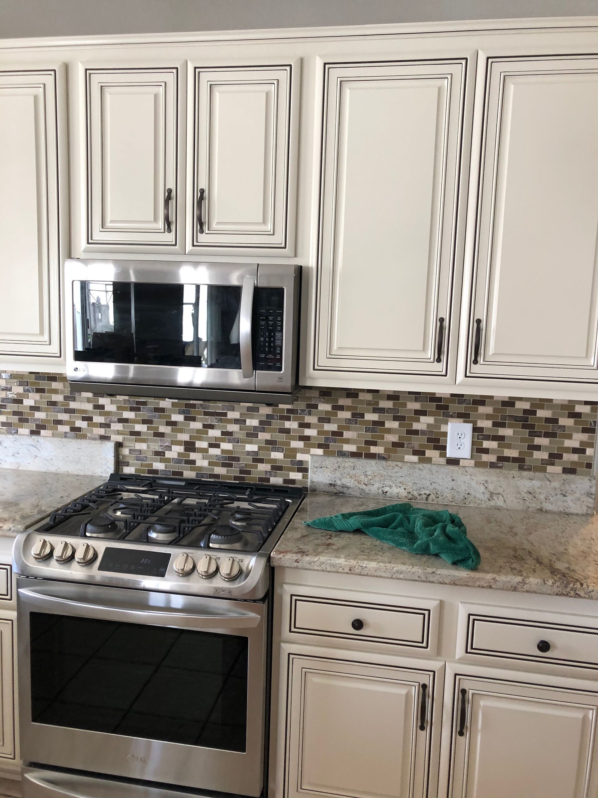 Kitchen with cream cabinets, stainless steel stove and microwave, granite countertop, and tiled backsplash