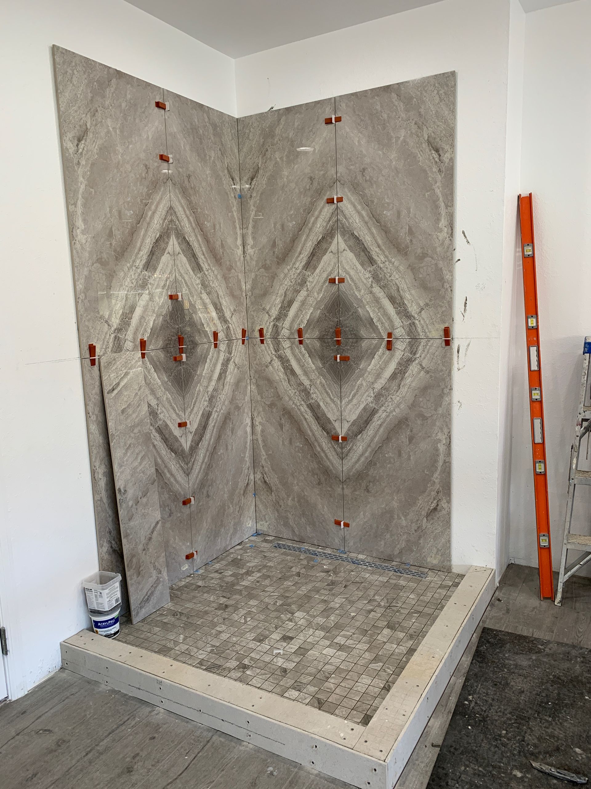 Shower alcove with gray patterned tile walls and floor, partially tiled in a bathroom under construction