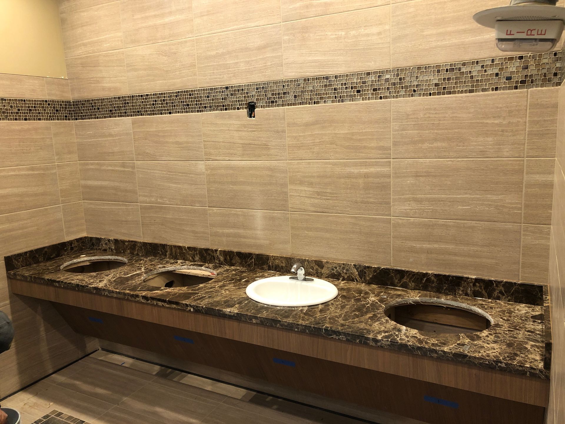 Restroom counter with white sink, black granite surface, and beige tiled wall with mirror kiosk above