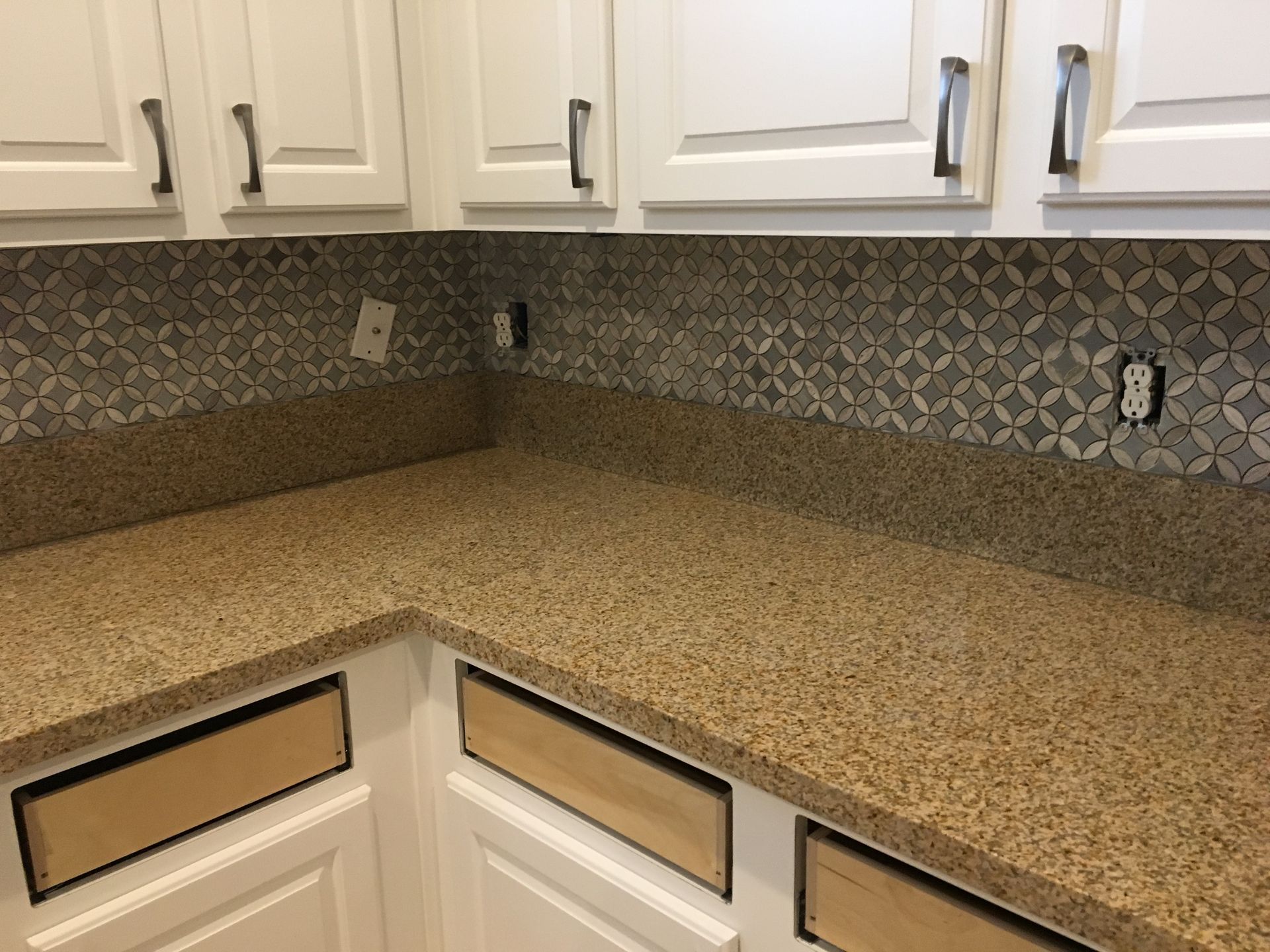 Corner kitchen counter with speckled beige countertop, white cabinets, and patterned backsplash