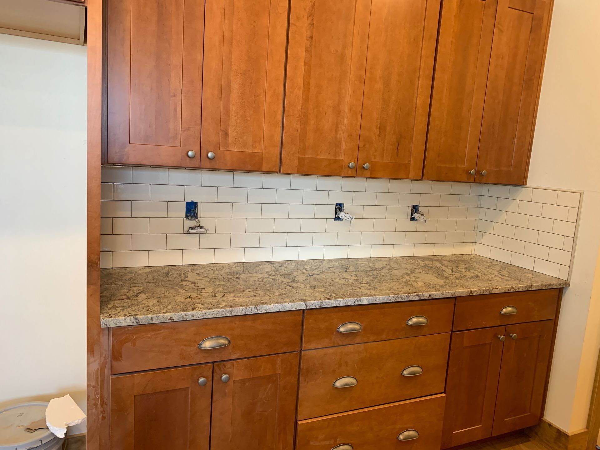 Kitchen cabinets with granite countertop, white subway tile backsplash, and wall outlets under upper wood cabinets