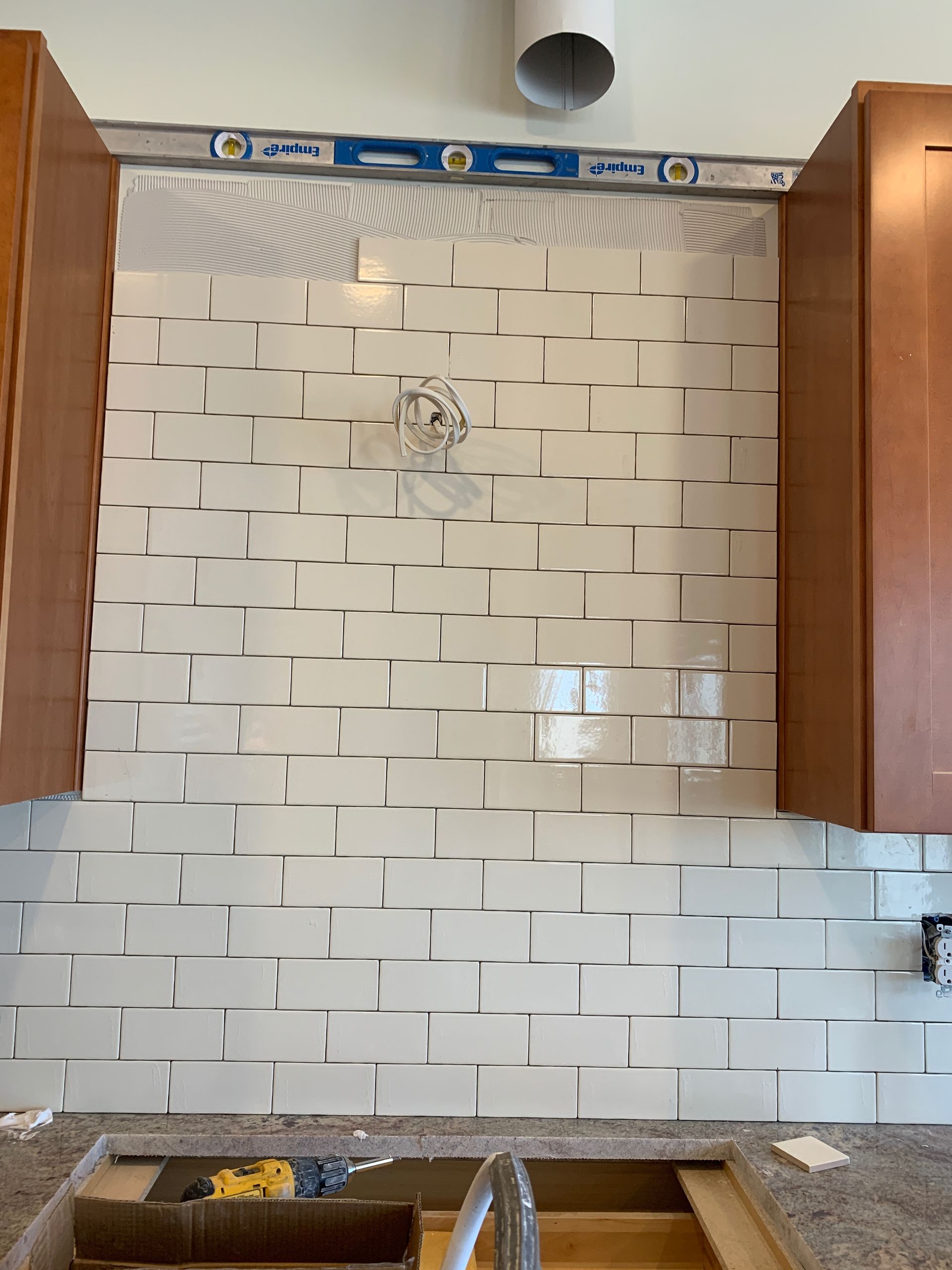 Kitchen backsplash with glossy white tile pattern, unfinished cabinets, and sink area under construction