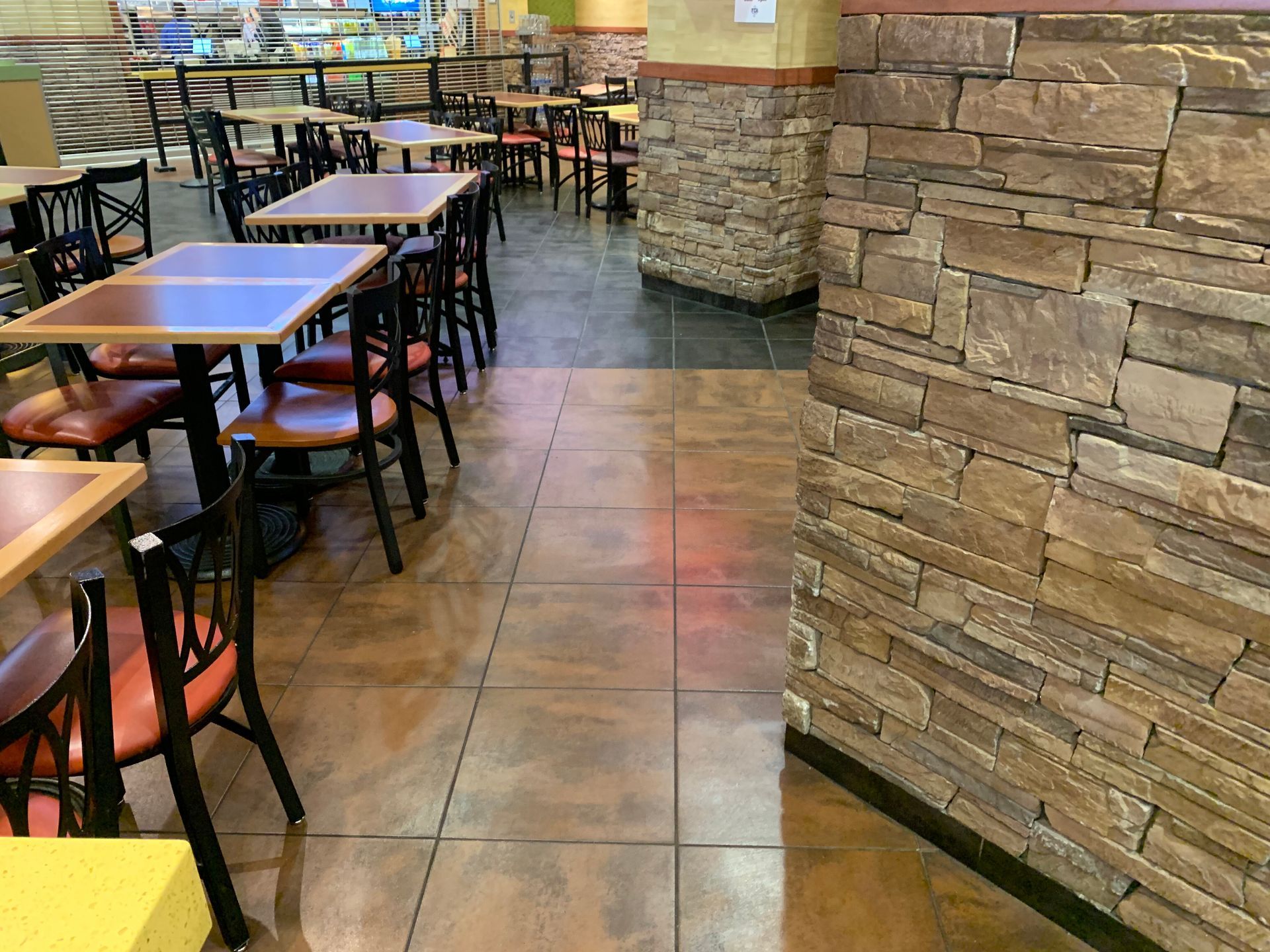 Empty restaurant dining area with tables and chairs beside a stone wall and tiled floor.