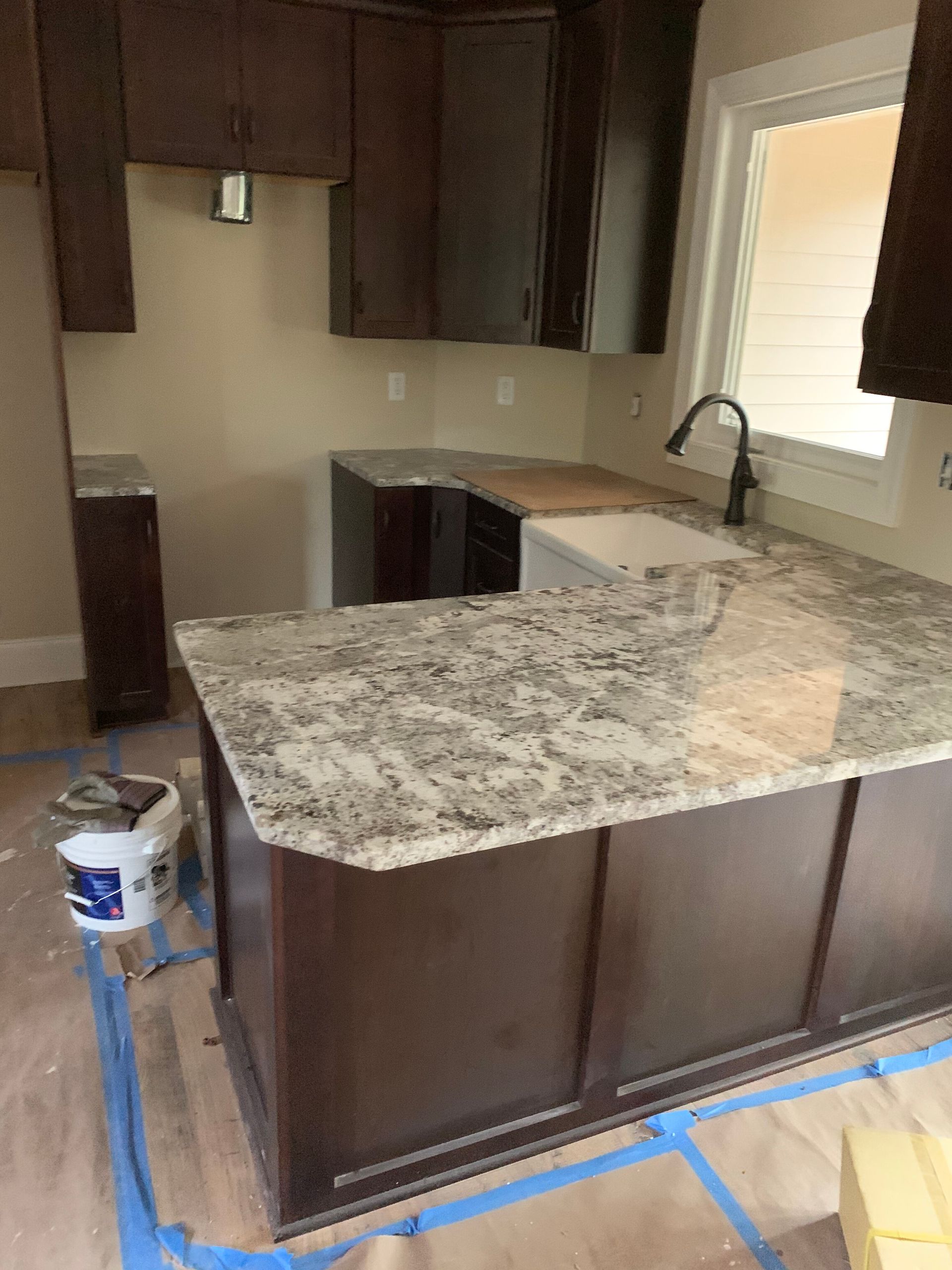 New kitchen with dark cabinets, speckled granite island, and blue painter’s tape on the floor