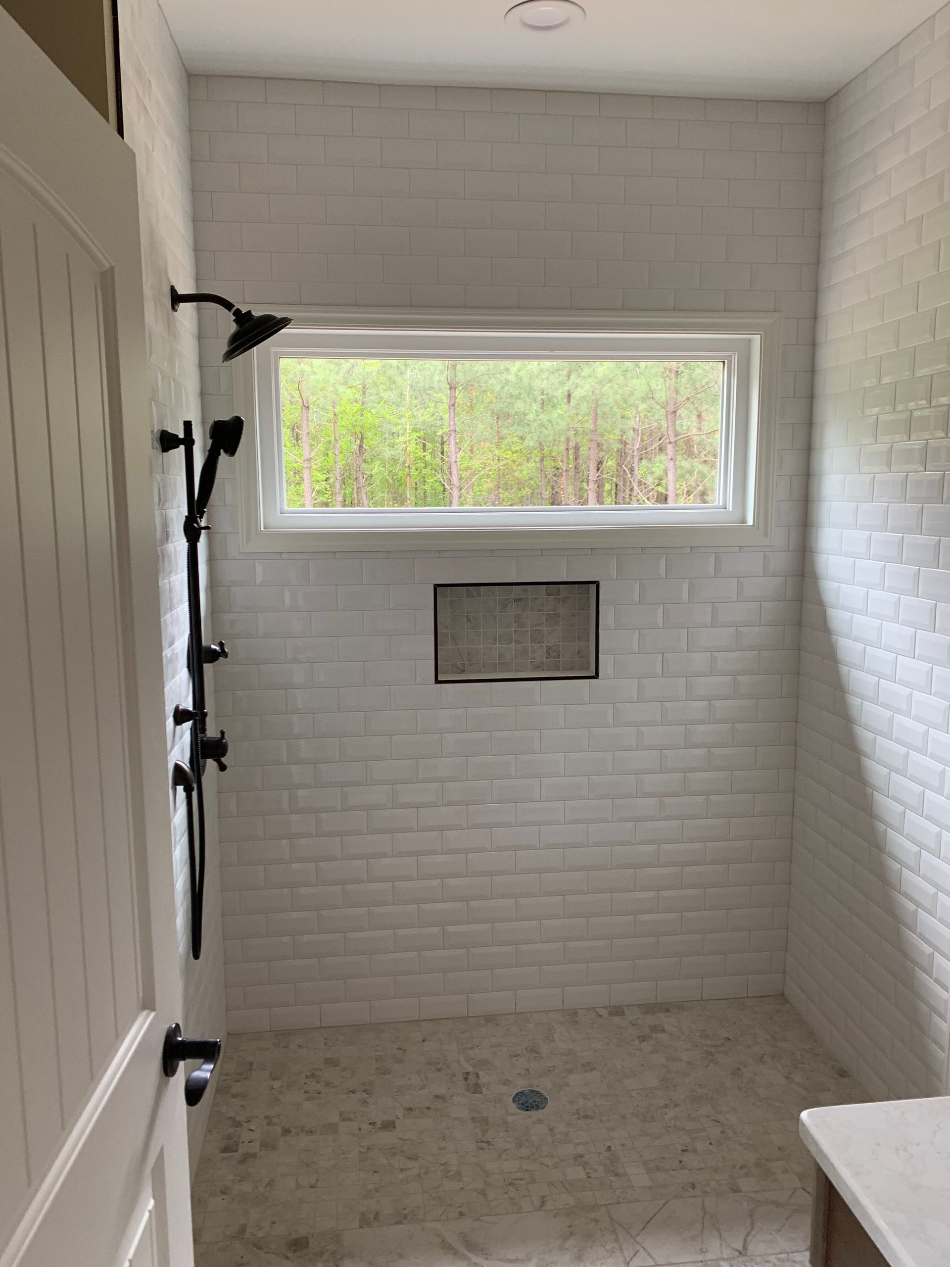 Empty white-tiled shower with window, built-in niche, and black shower fixtures