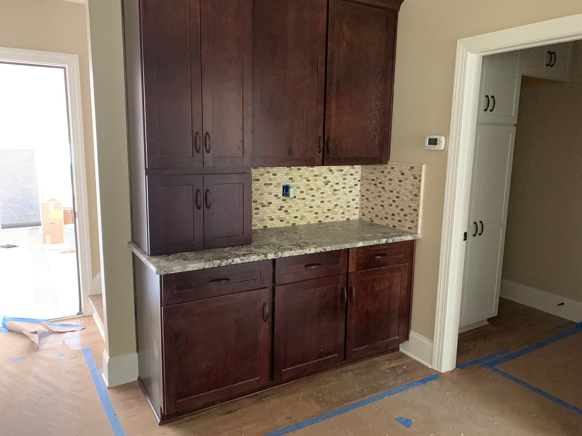 Built-in dark wood cabinets and granite counter in a home hallway, with tile backsplash and open doorways nearby