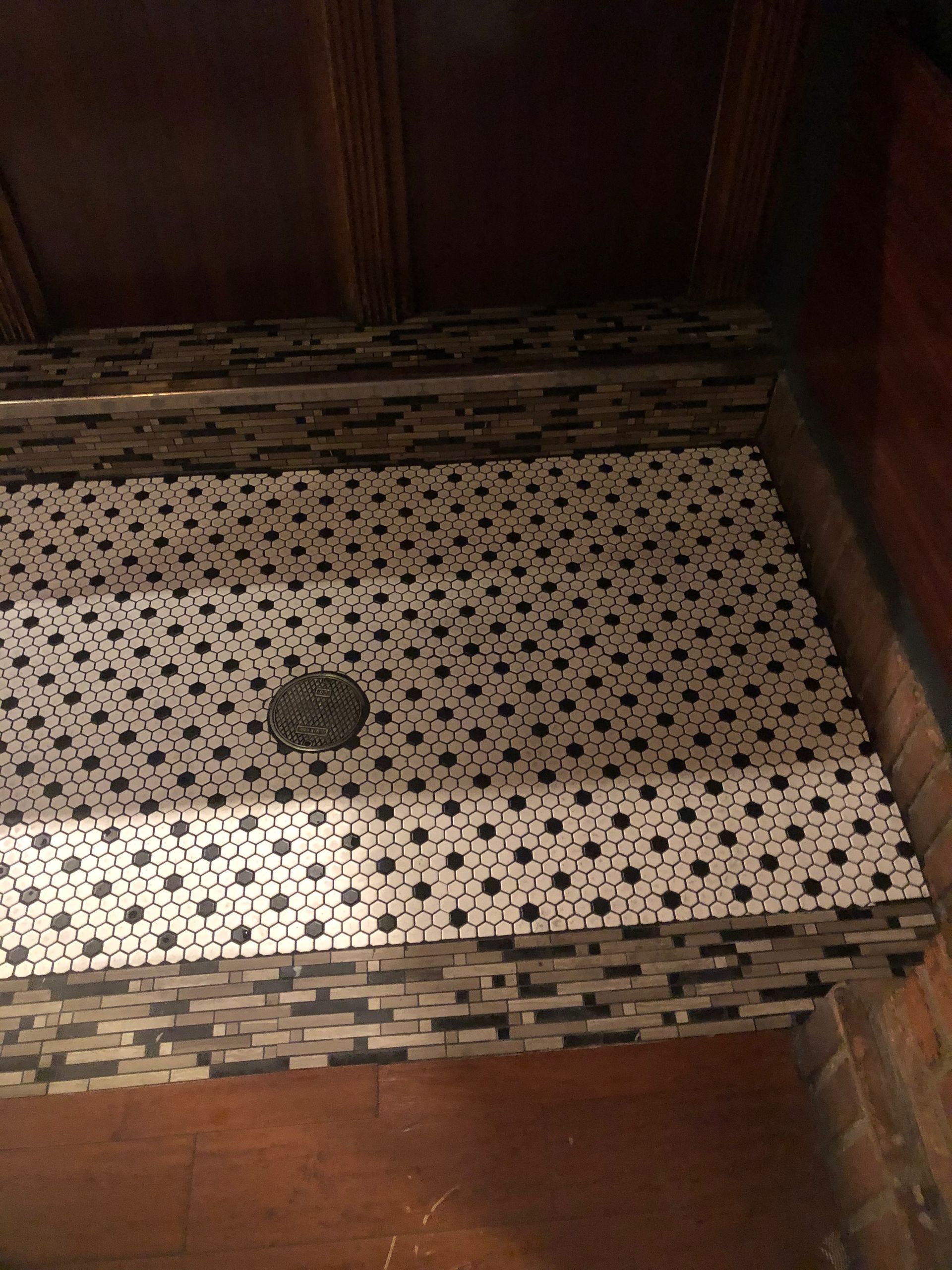 Patterned tile floor in a doorway or shower threshold with a central drain, bordered by wood panels.