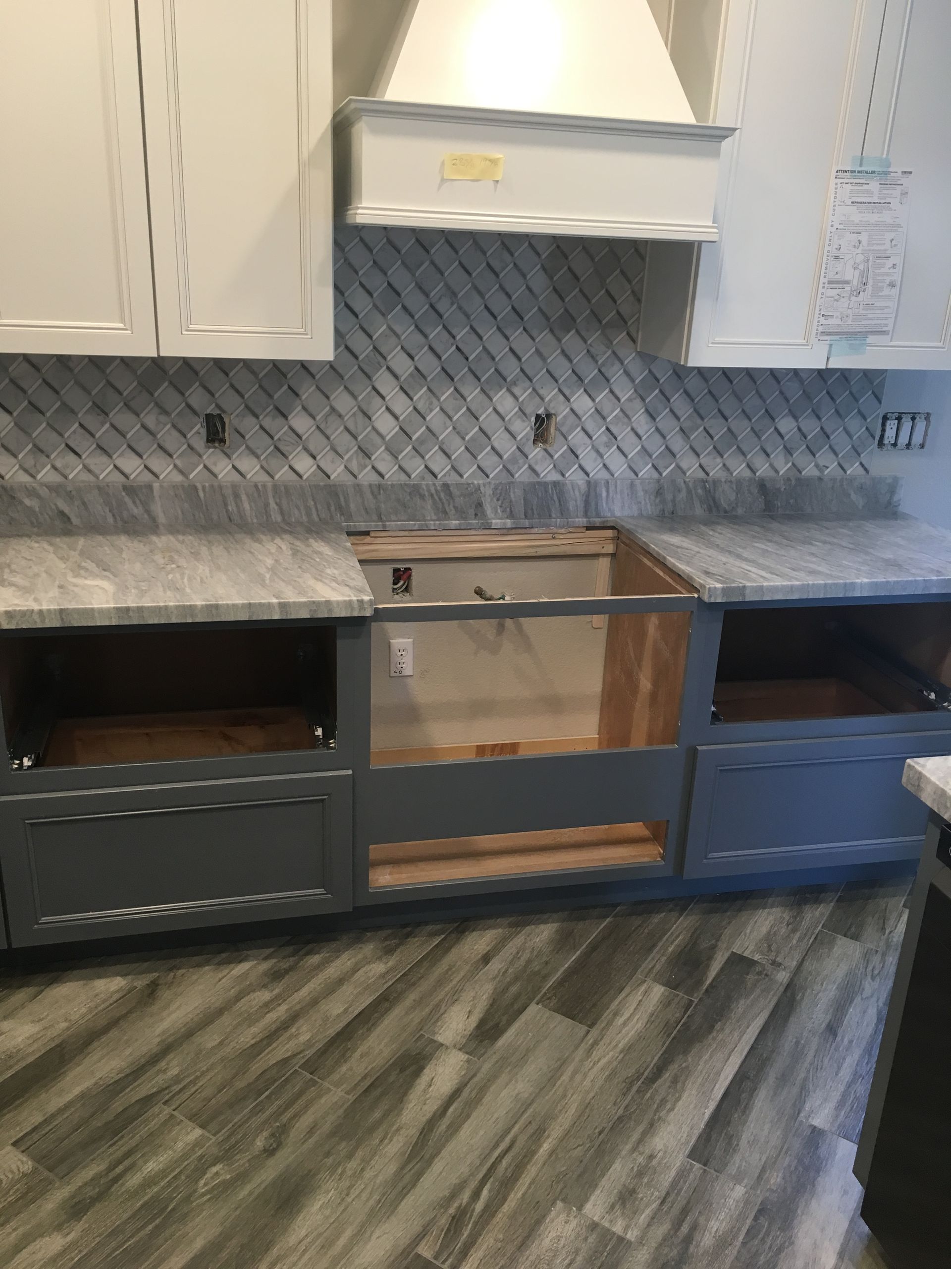 Kitchen cabinets under installation with open dark and blue base units, white uppers, and a gray tile backsplash.