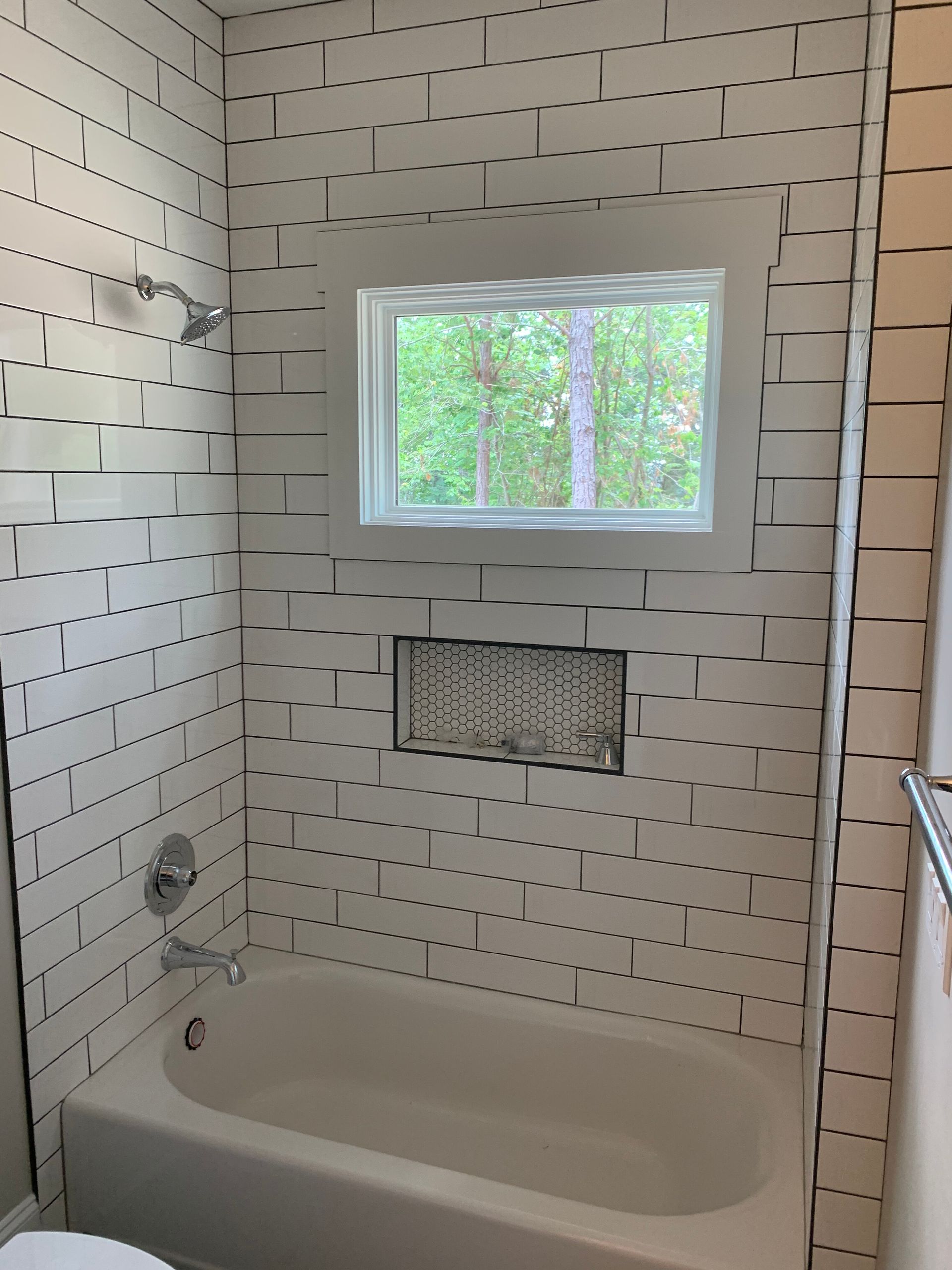 Small bathroom with a tiled shower and tub, a window, and a recessed wall niche.