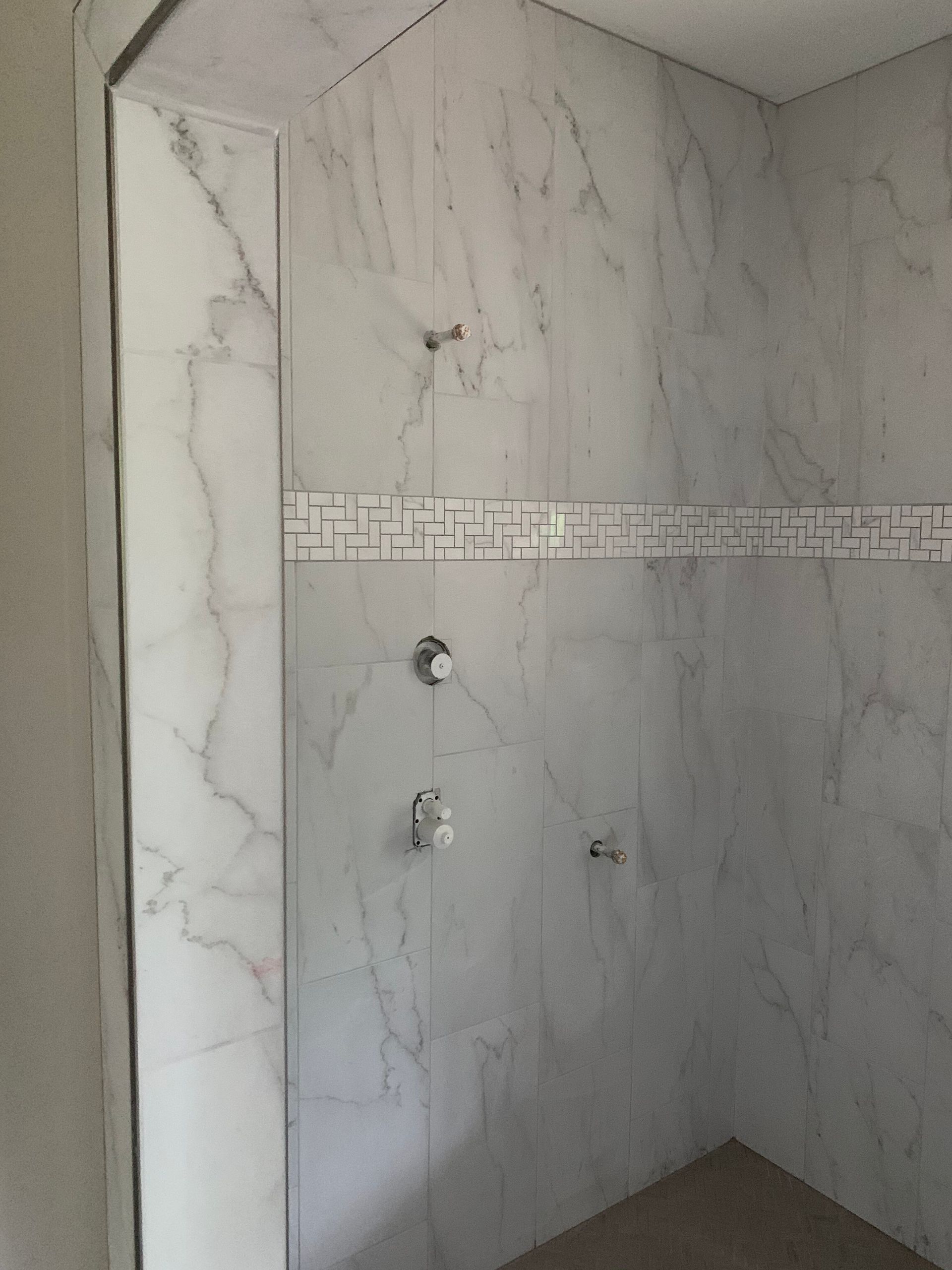 Marble-tiled shower with chrome fixtures and decorative border trim