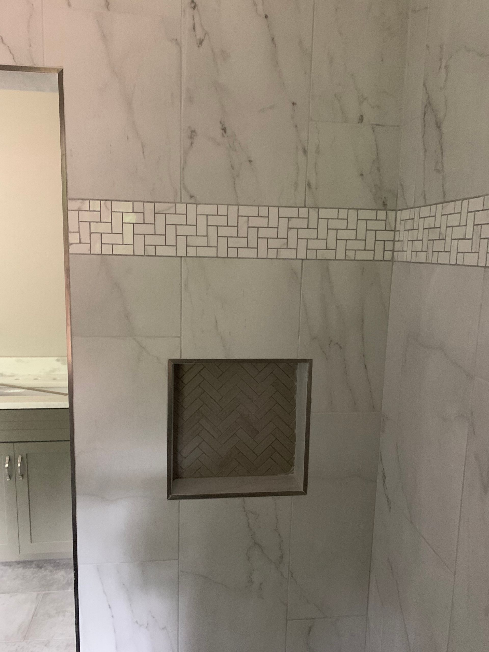 Marble-tiled wall with a horizontal mosaic strip and a small square recessed niche