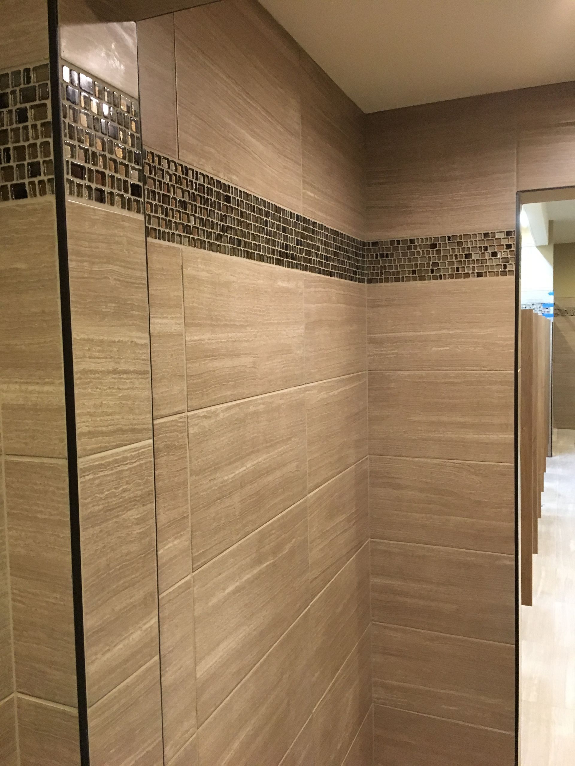 Tiled restroom stall wall with beige tiles and a dark mosaic border