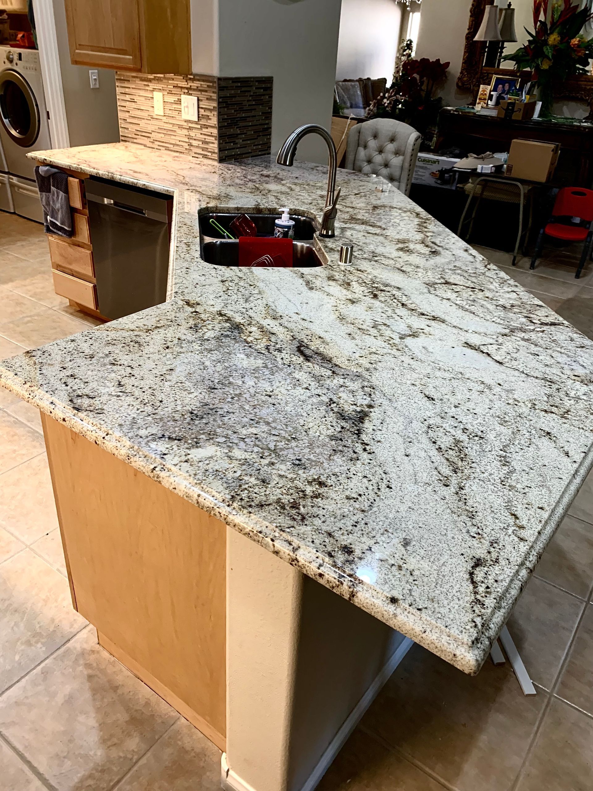 Granite kitchen island with sink and faucet in a tiled home interior, viewed from the side