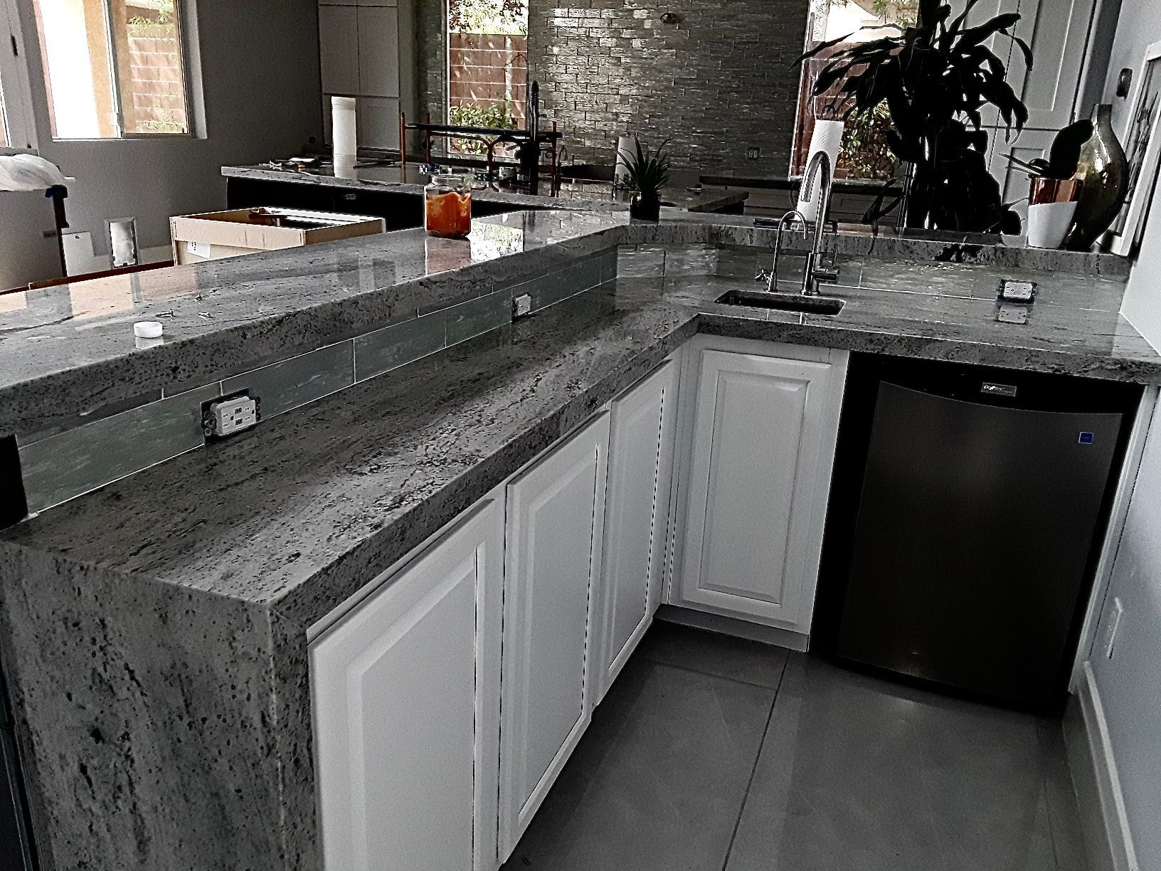 Modern kitchen corner with gray granite countertops, white cabinets, and a black mini fridge under the counter