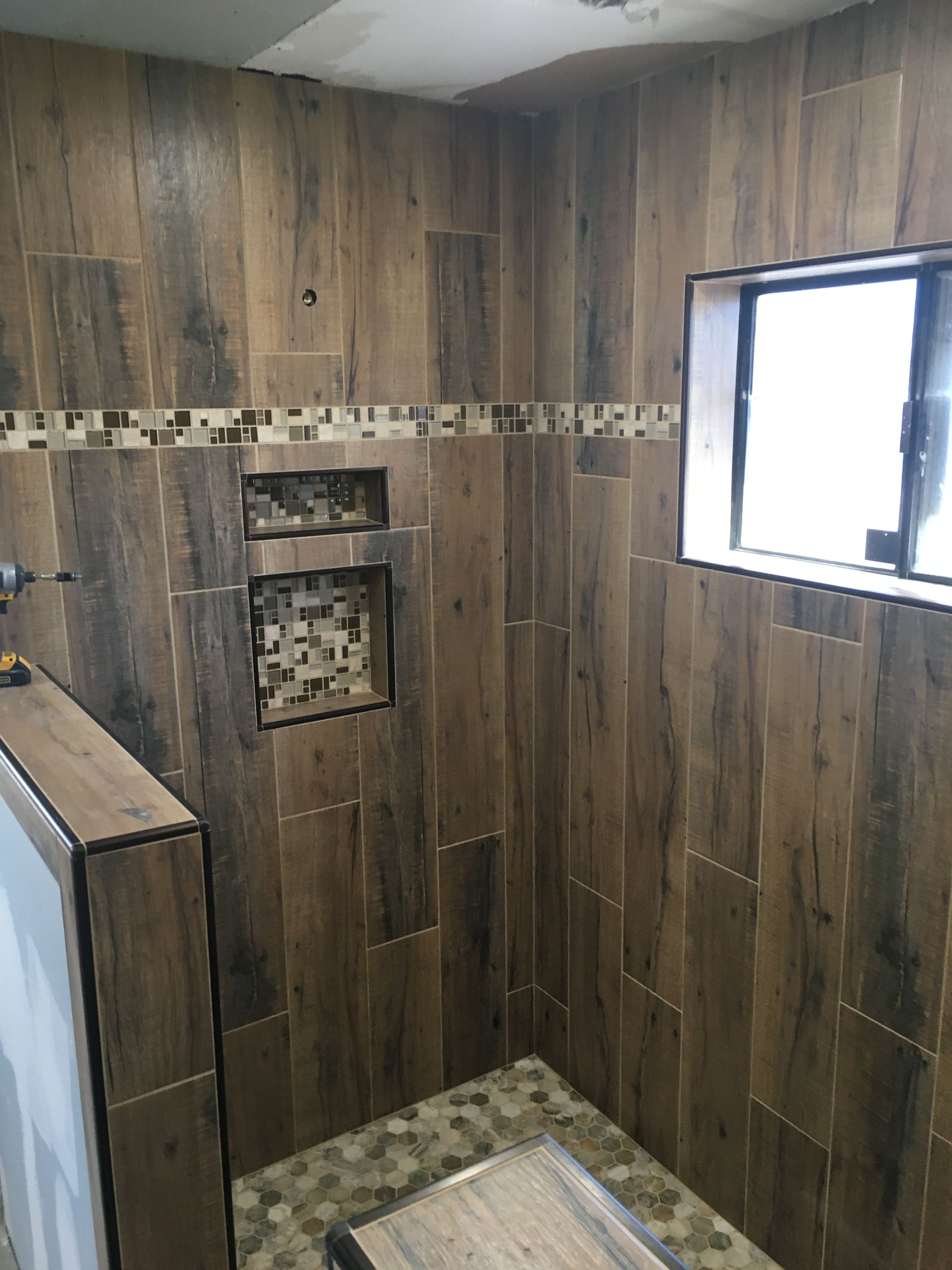 Small tiled shower stall with wood-look walls, a window, and built-in shelves.