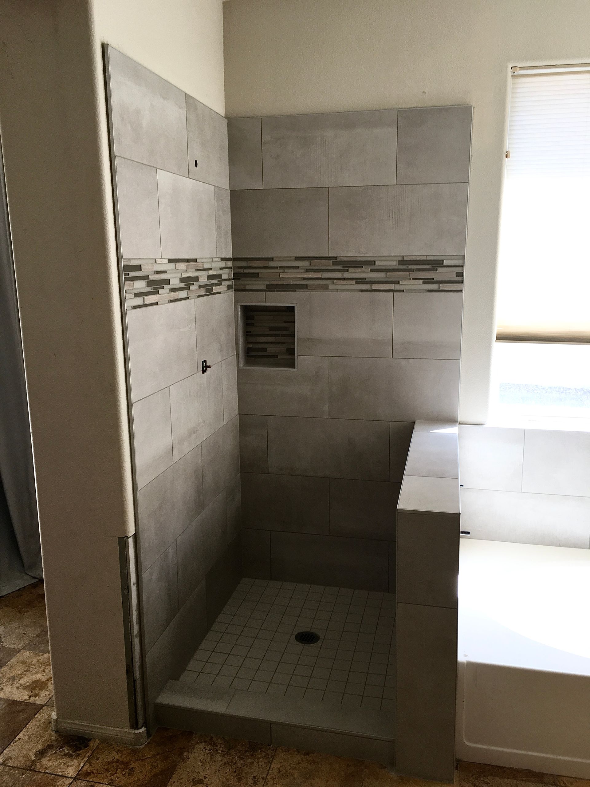 Bathroom with a white built-in soaking tub beside a window and tiled walls