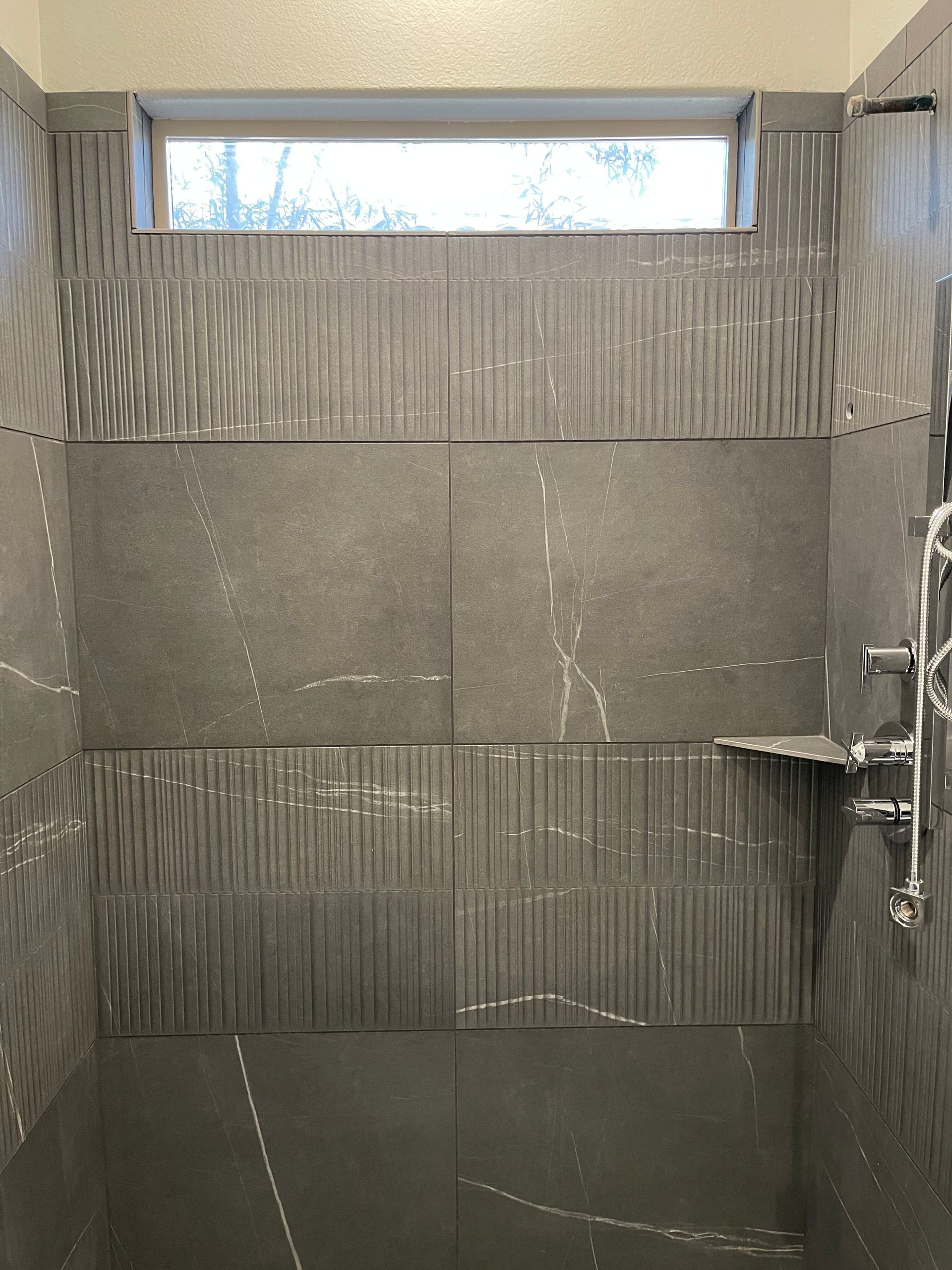 Small tiled shower stall with a narrow frosted window and chrome fixtures