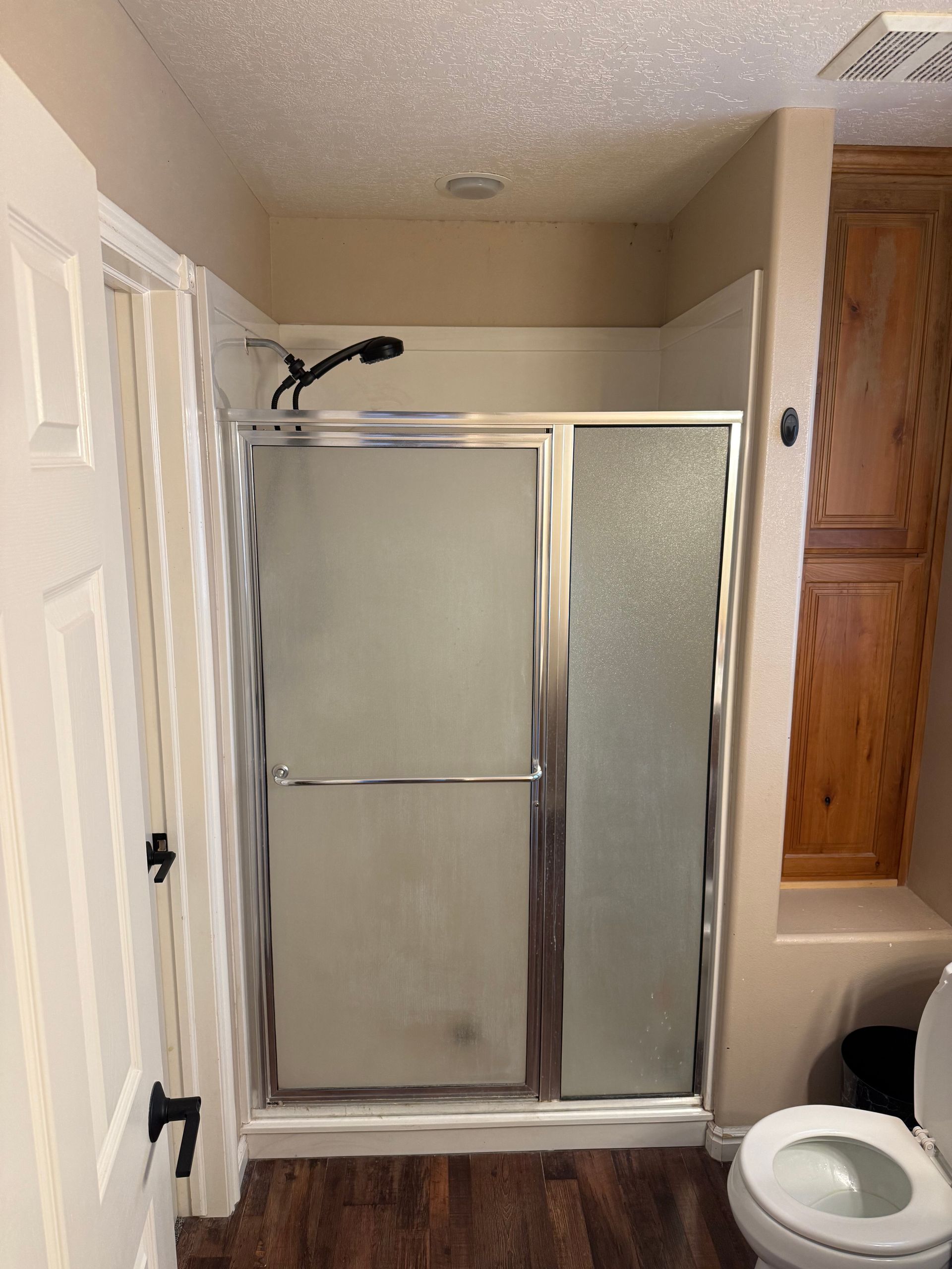 Bathroom with frosted glass shower doors, toilet, and beige walls.