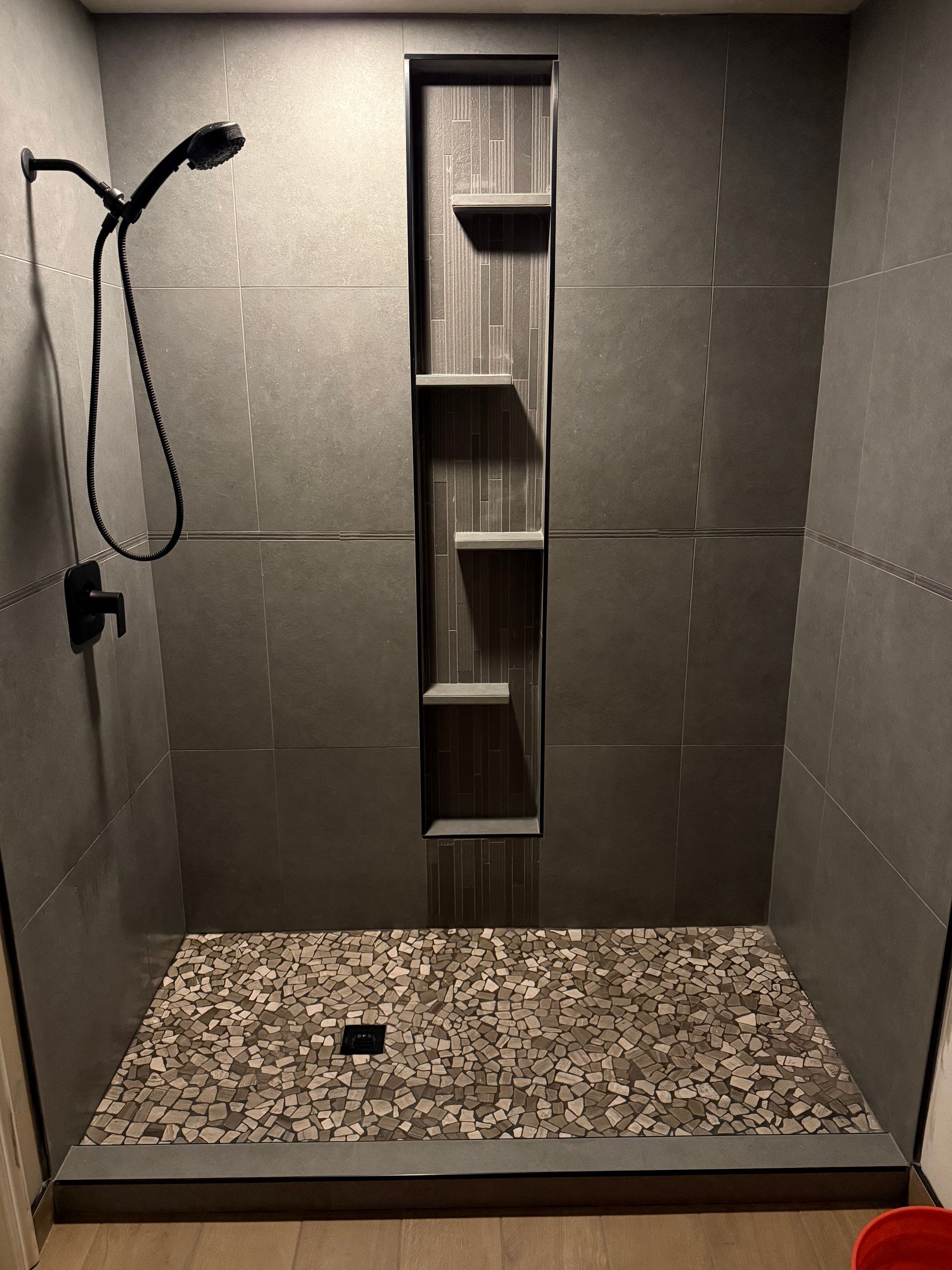 Modern tiled shower with a handheld showerhead and built-in recessed shelf niche.