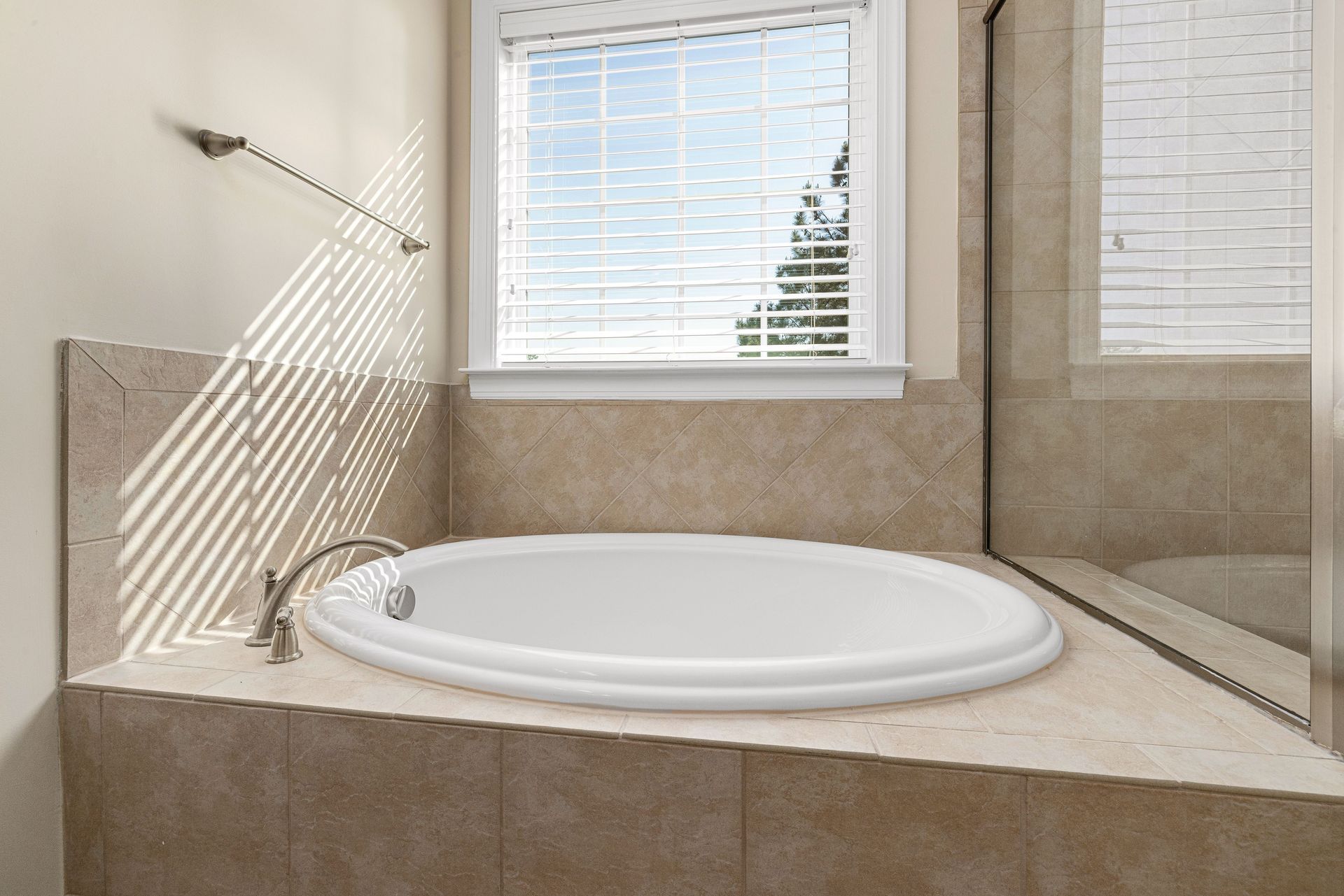 Bathroom with a white built-in soaking tub beside a window and tiled walls