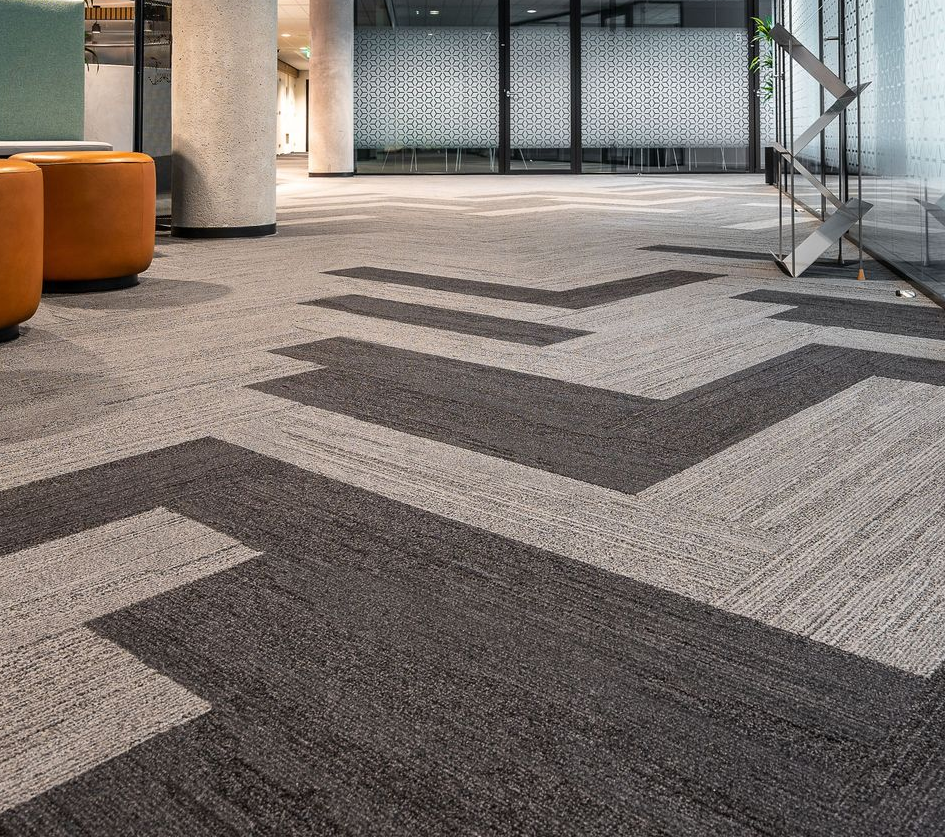 Modern lobby with gray chevron-pattern carpet, orange seating, and glass walls