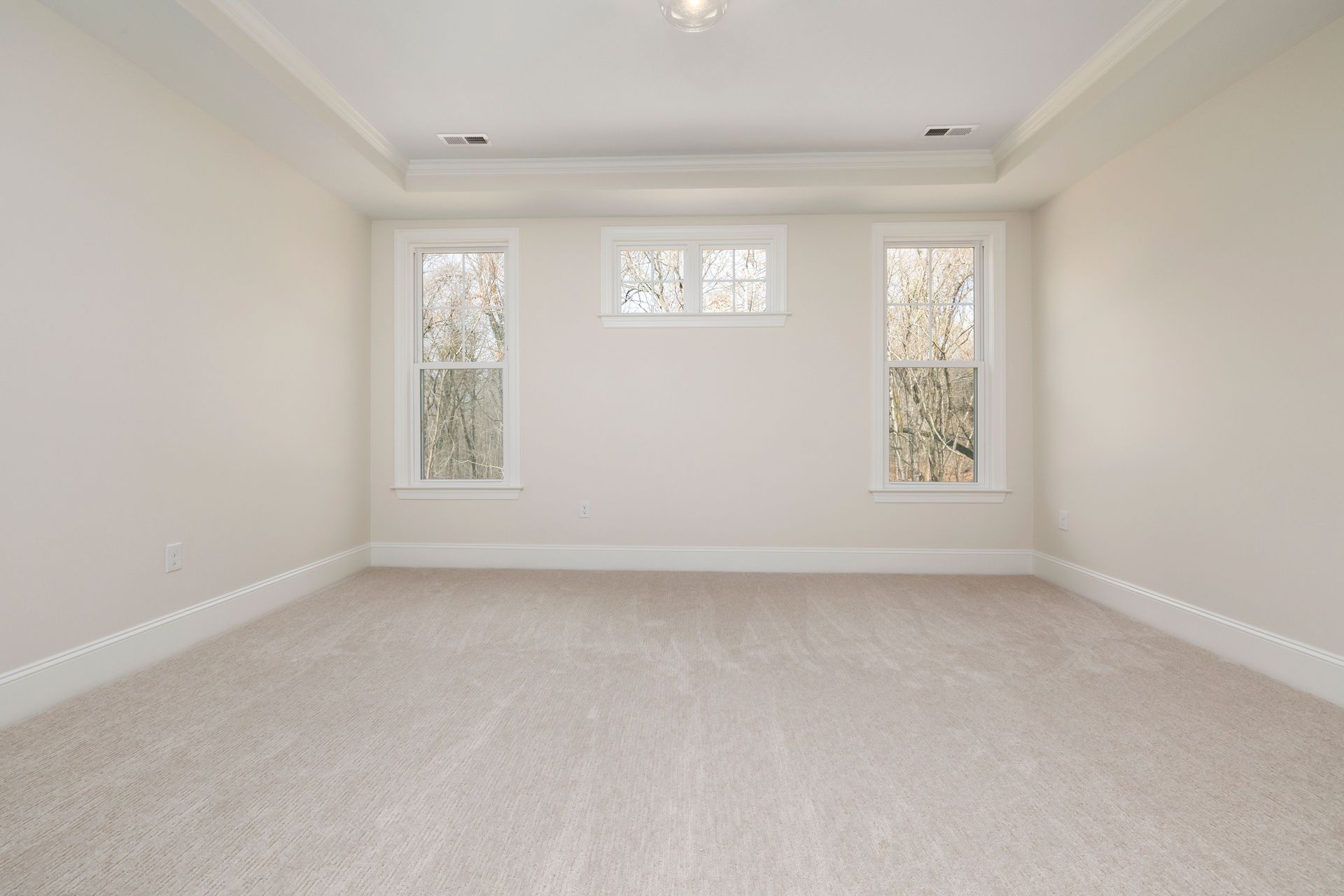 Empty carpeted living room with white walls and three windows letting in natural light