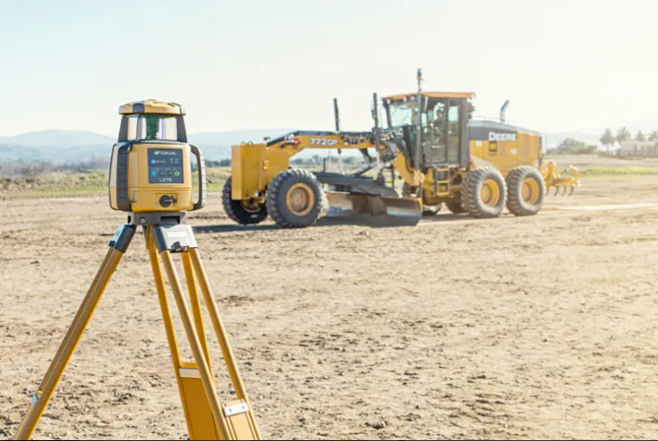Yellow Survey Equipment on Tripod in Foreground, With a Road Grader — Coastal Surveying Group Pty Ltd In Baringa, QLD