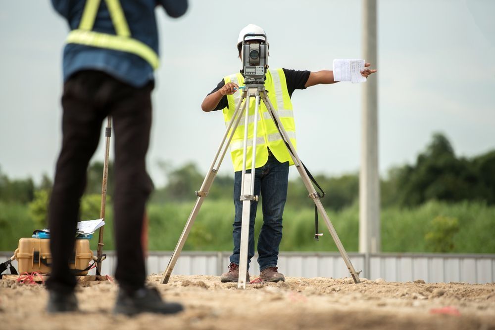 Surveyor in a Yellow Vest Using a Tripod-mounted Instrument — Coastal Surveying Group Pty Ltd In Gympie, QLD