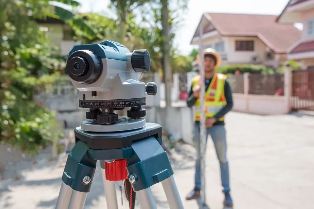 Surveying Equipment on a Tripod With a Worker in a Safety Vest — Coastal Surveying Group Pty Ltd In Moreton Bay, QLD