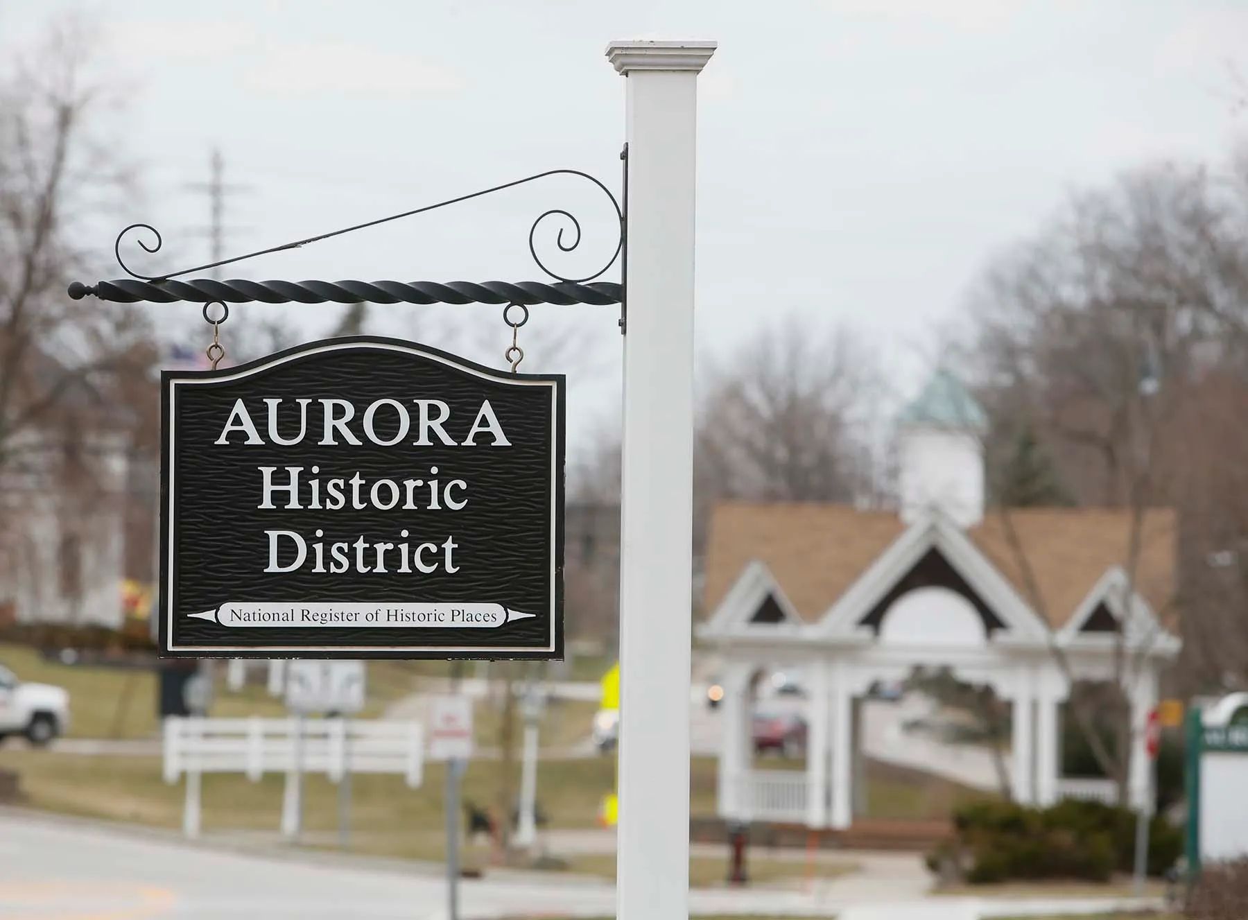 Sign for Aurora Historic District on a white post, with houses blurred in the background