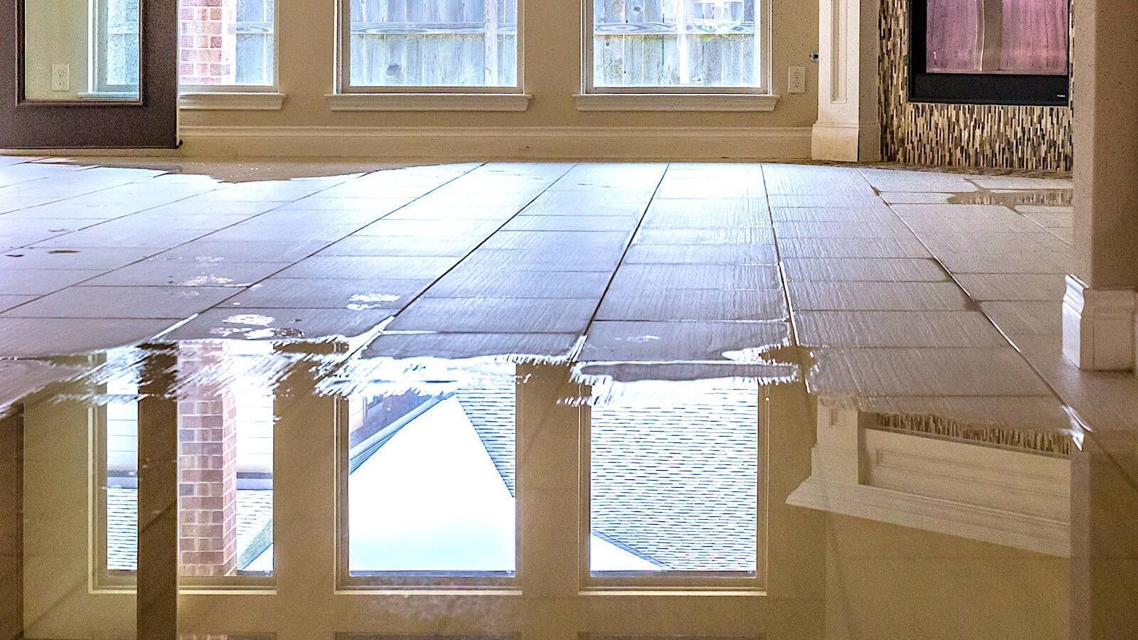 Empty tiled room with a large puddle reflecting windows and the ceiling.