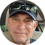 Close-up portrait of a smiling man wearing a black cap and sunglasses, outdoors.